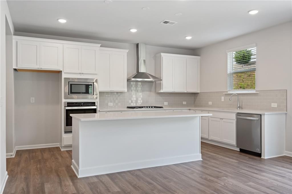 Bright modern kitchen with white cabinets, large island, stainless appliances, subway backsplash, hardwood floors in Davidson Homes The Hickory A, Winder, GA