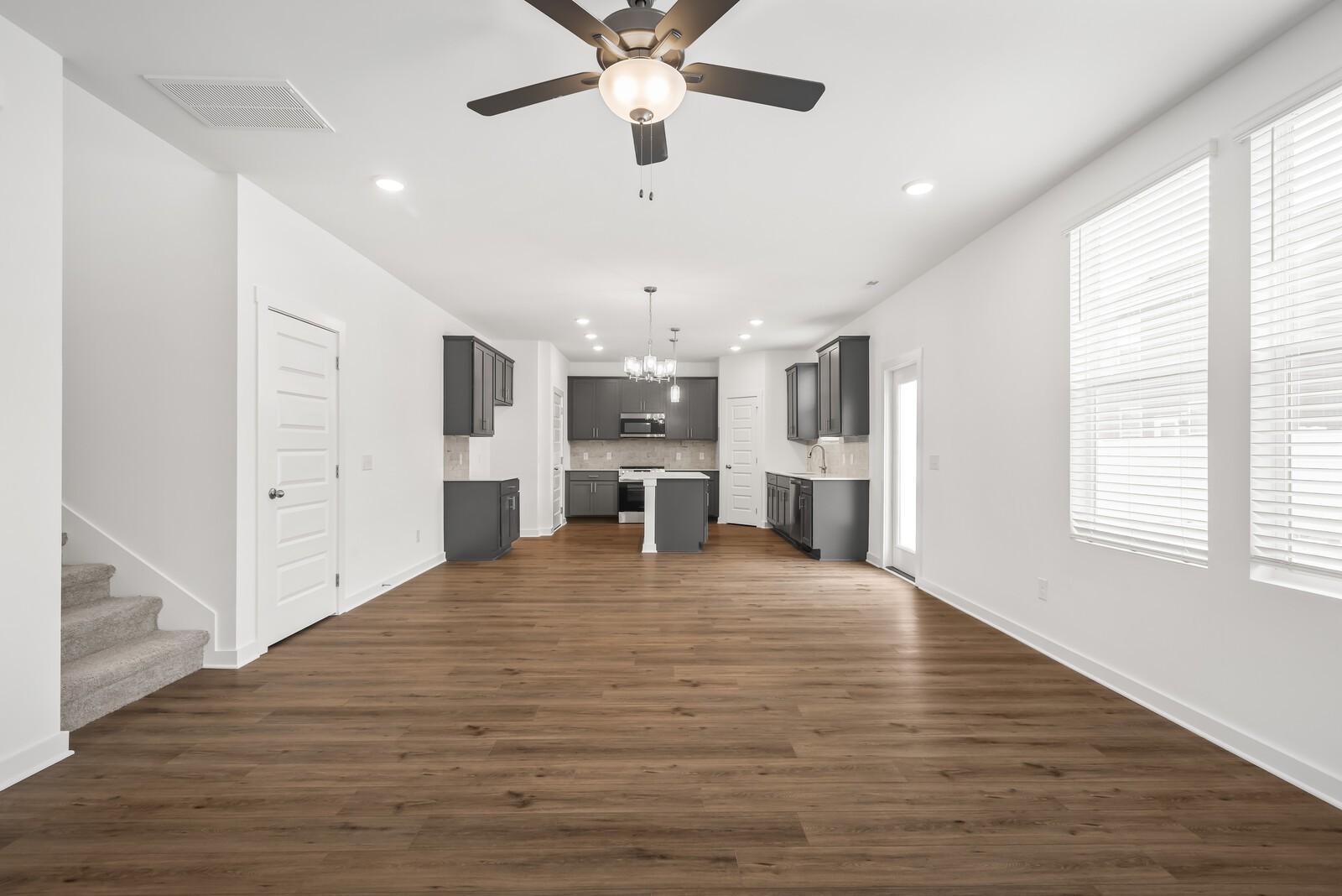 Open-concept kitchen and living space with gray cabinets, island, hardwood floors, and ceiling fan in Davidson Homes The Gordon C, White House, TN