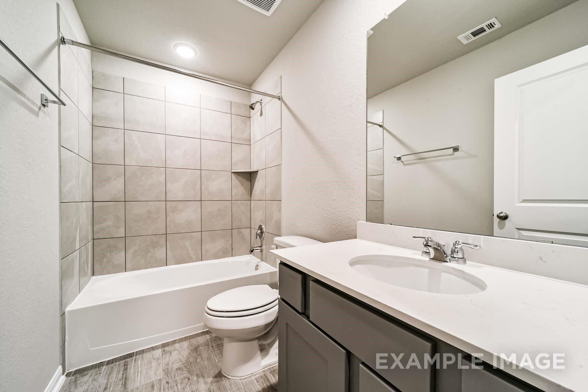 Modern bathroom with tiled shower-tub combo and gray vanity in The Riviera A floor plan at Emberly, Beasley, Texas.