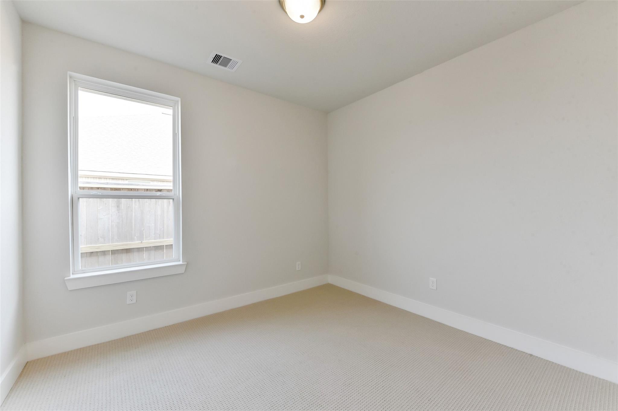 Spacious empty bedroom with beige carpet, white walls, large window, and neutral tones in Davidson Homes The Edward A, Lago Mar, Texas City