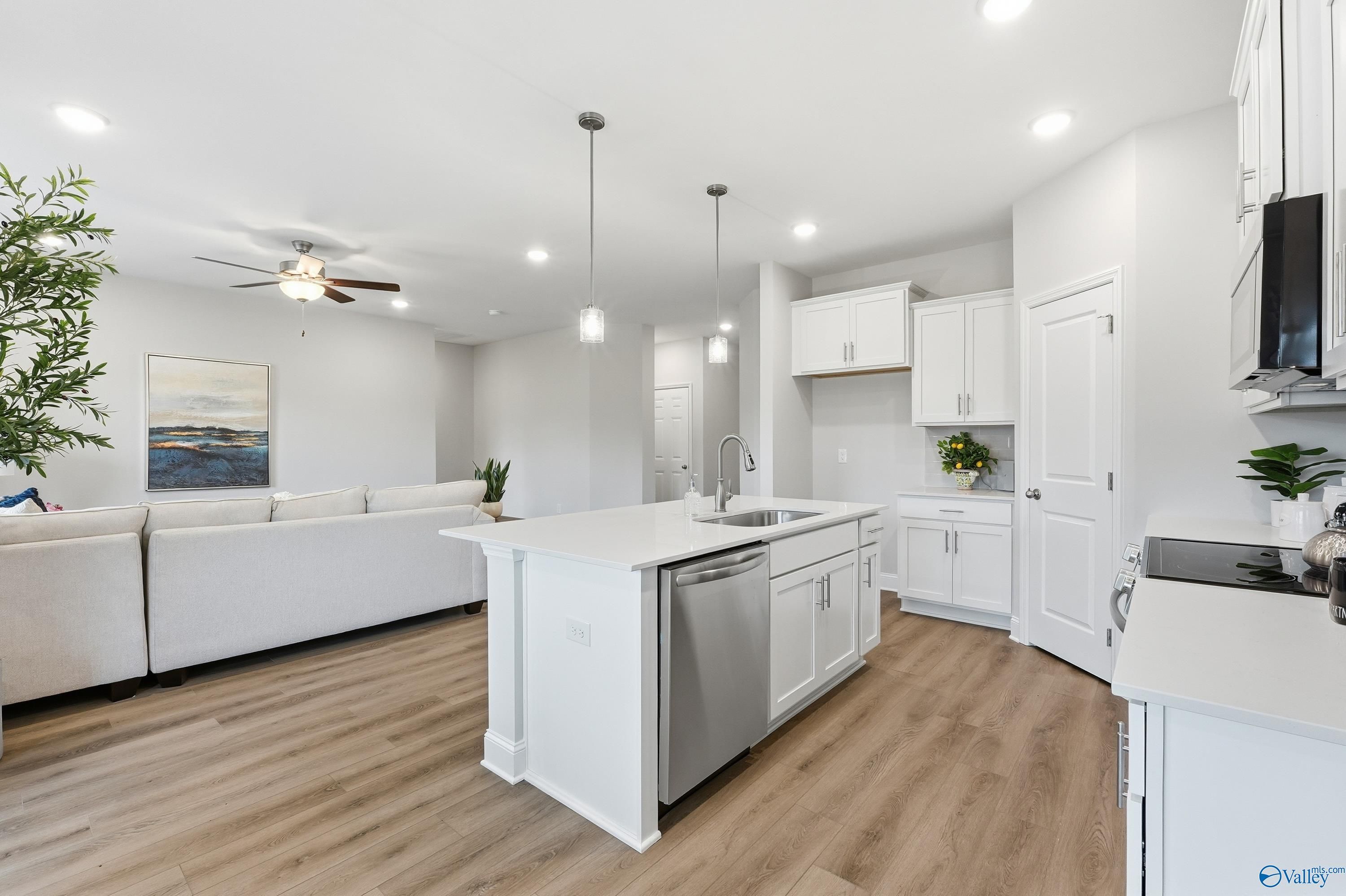 Open-concept living room and kitchen with white island, pendant lights, ceiling fan, and sofa in The Asheville by Davidson Homes, Toney, Alabama