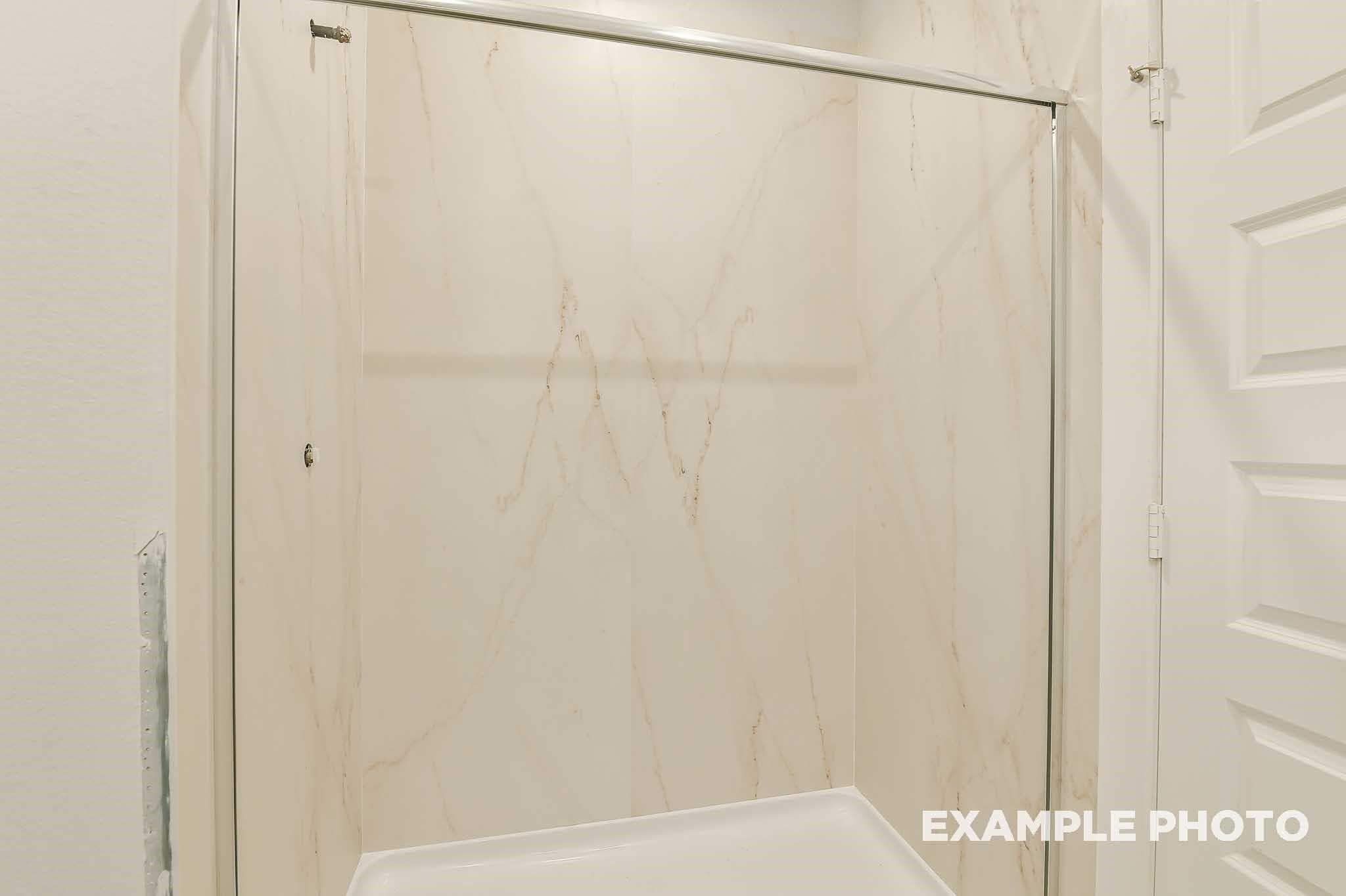 Modern glass shower enclosure with marble-patterned tile walls in secondary bath, Davidson Homes The Colorado F, Conroe, Texas