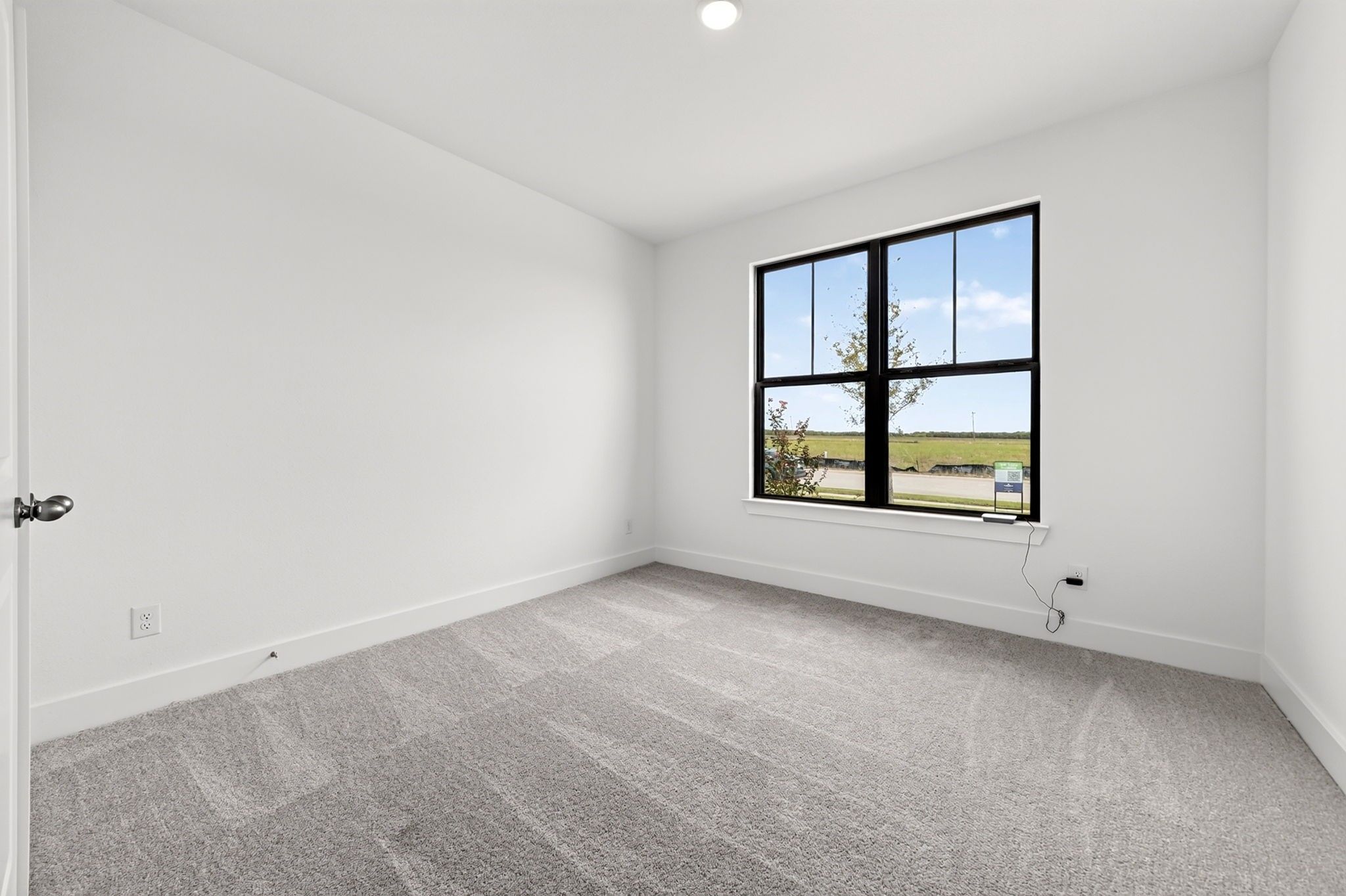 Bright empty bedroom with carpet, white walls, and black-framed window in Davidson Homes Holly F plan, Meadow Ridge Estates, Texas