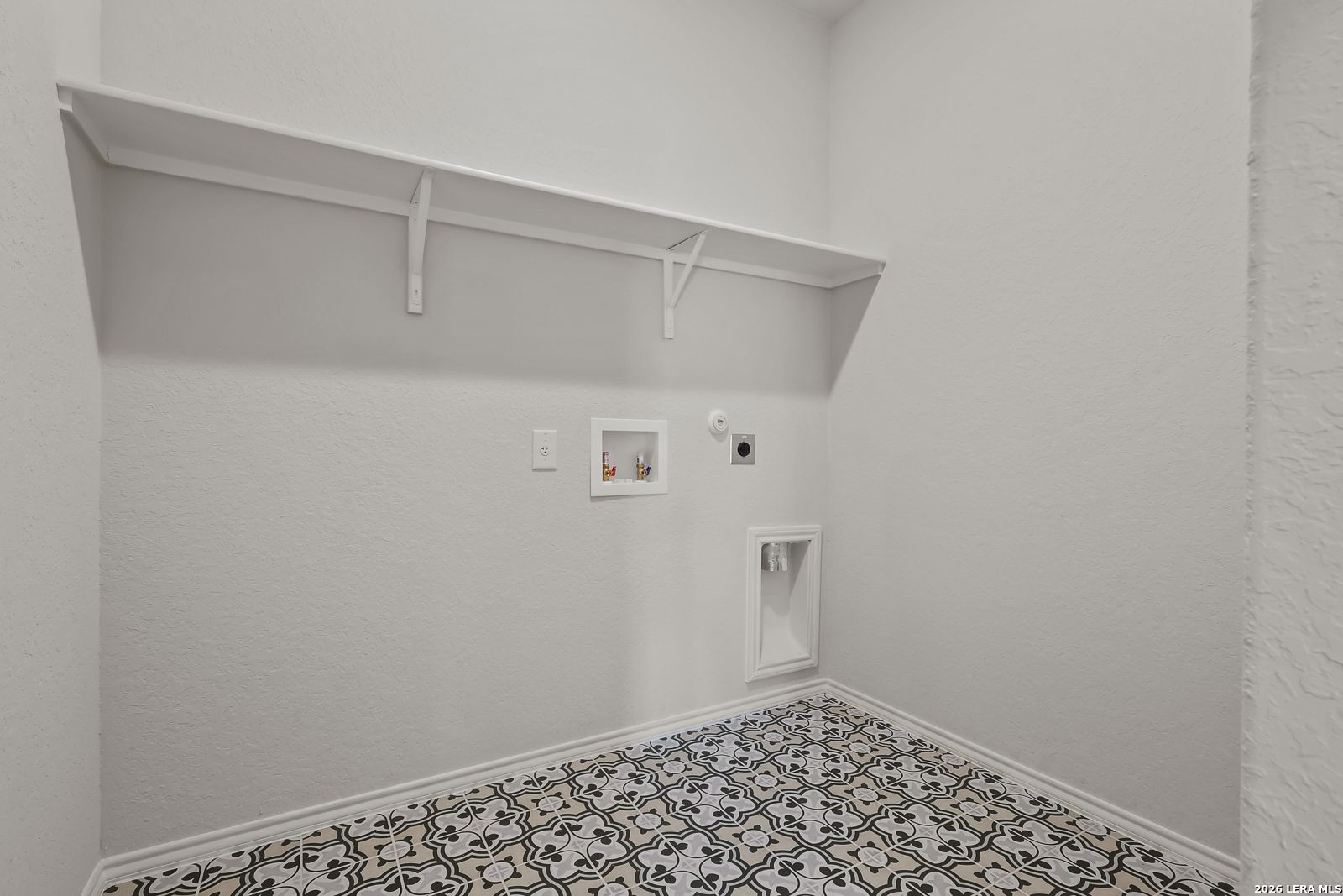 Bright laundry room with open shelving, washer-dryer hookups, and patterned tile floor in The Daphne H, Hannah Heights, Seguin, Texas