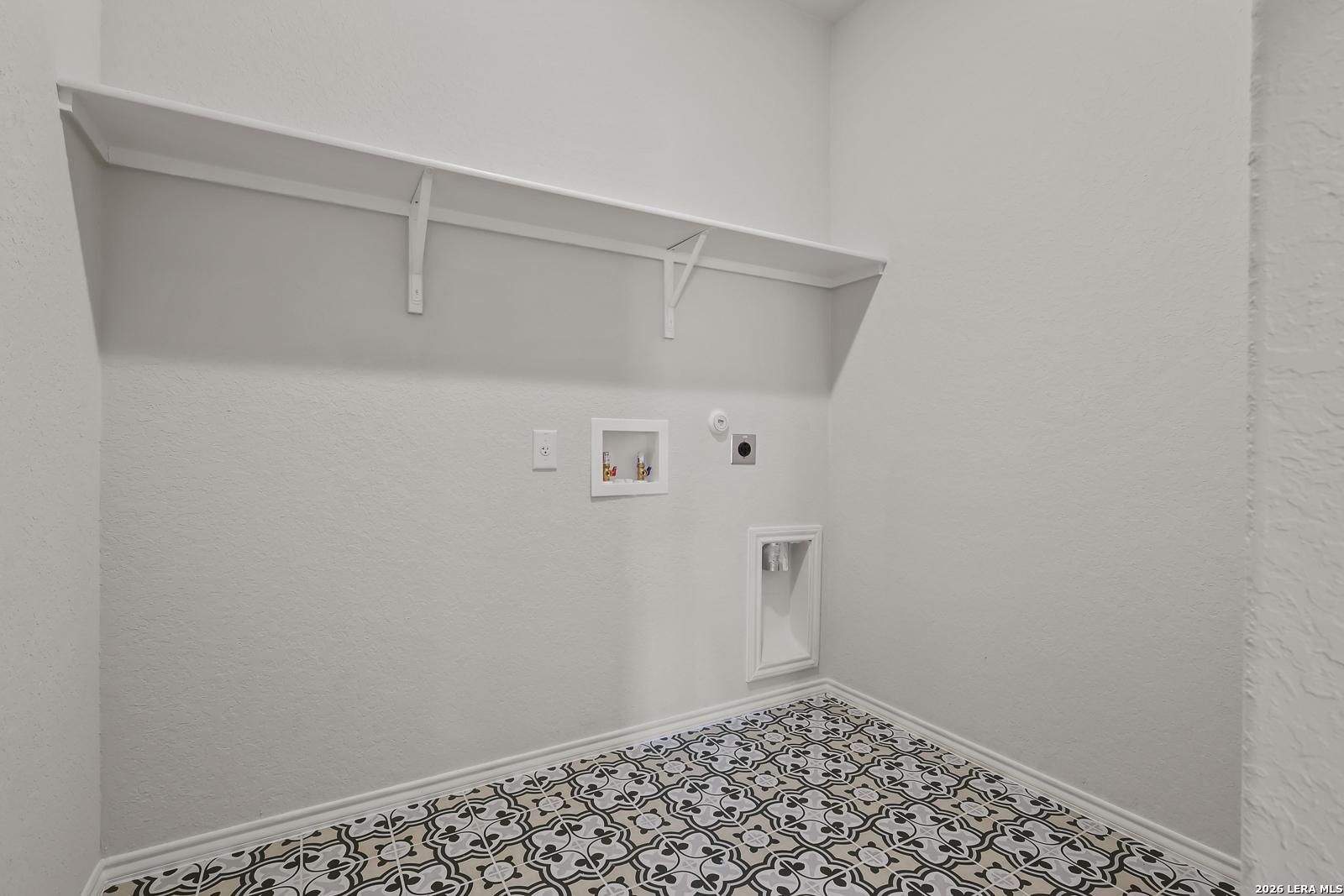Bright laundry room with open shelving, washer-dryer hookups, and patterned tile floor in The Daphne H, Hannah Heights, Seguin, Texas