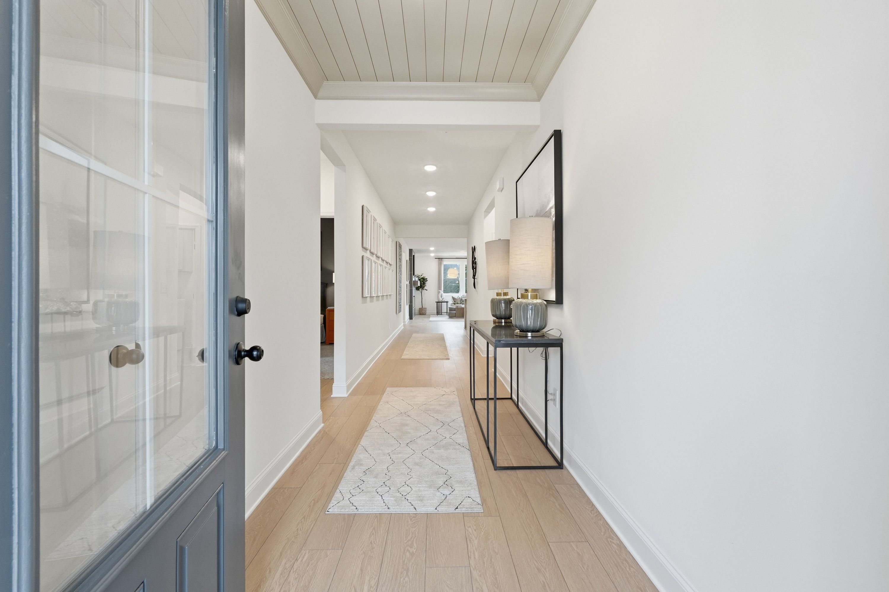 Spacious entryway hallway in The Laurel K home with glass front door, hardwood floors, runner rug, console table, and wall art