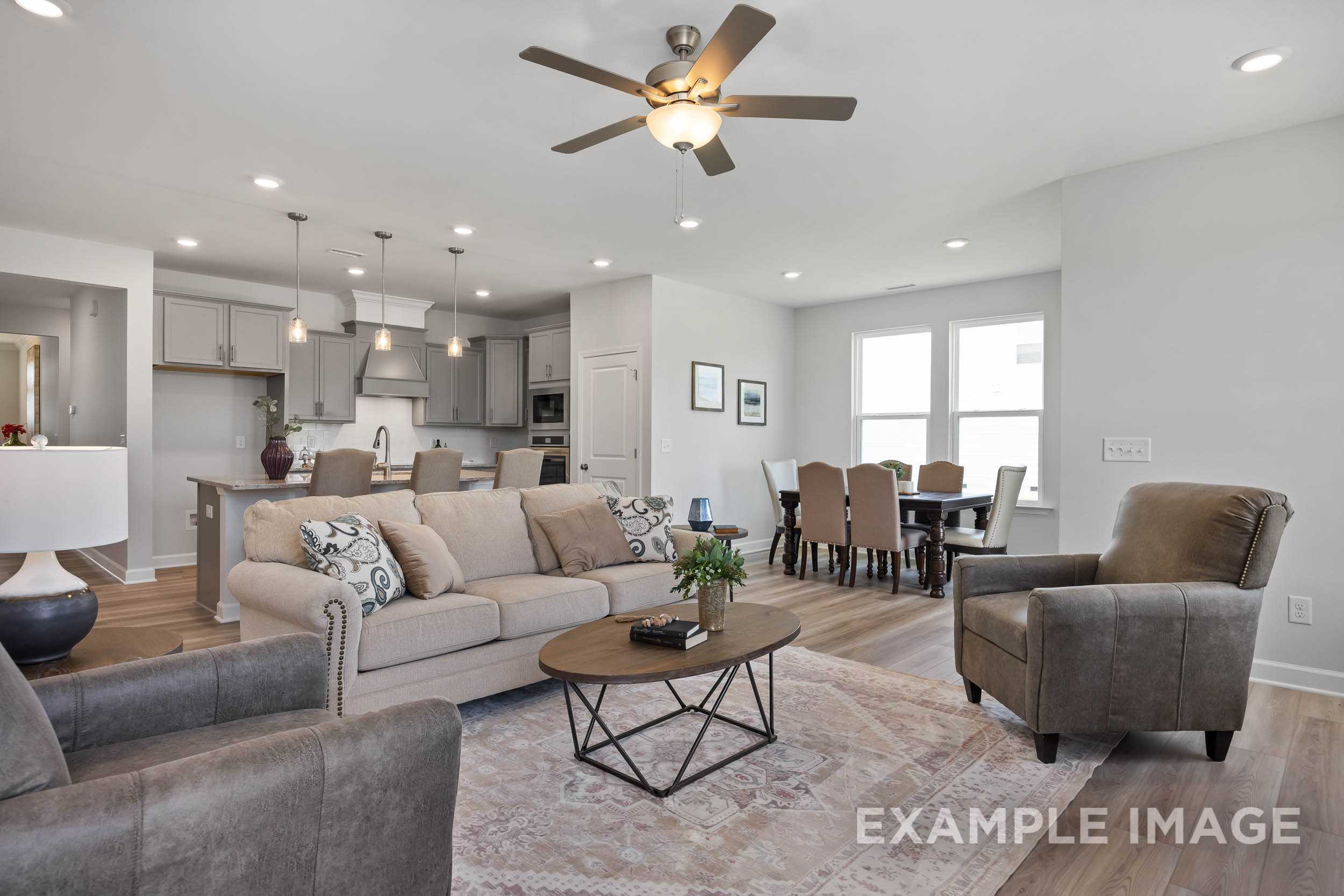 Spacious open-concept living and dining area in The Daphne C with gray sofa, wooden table, kitchen island, and ceiling fan