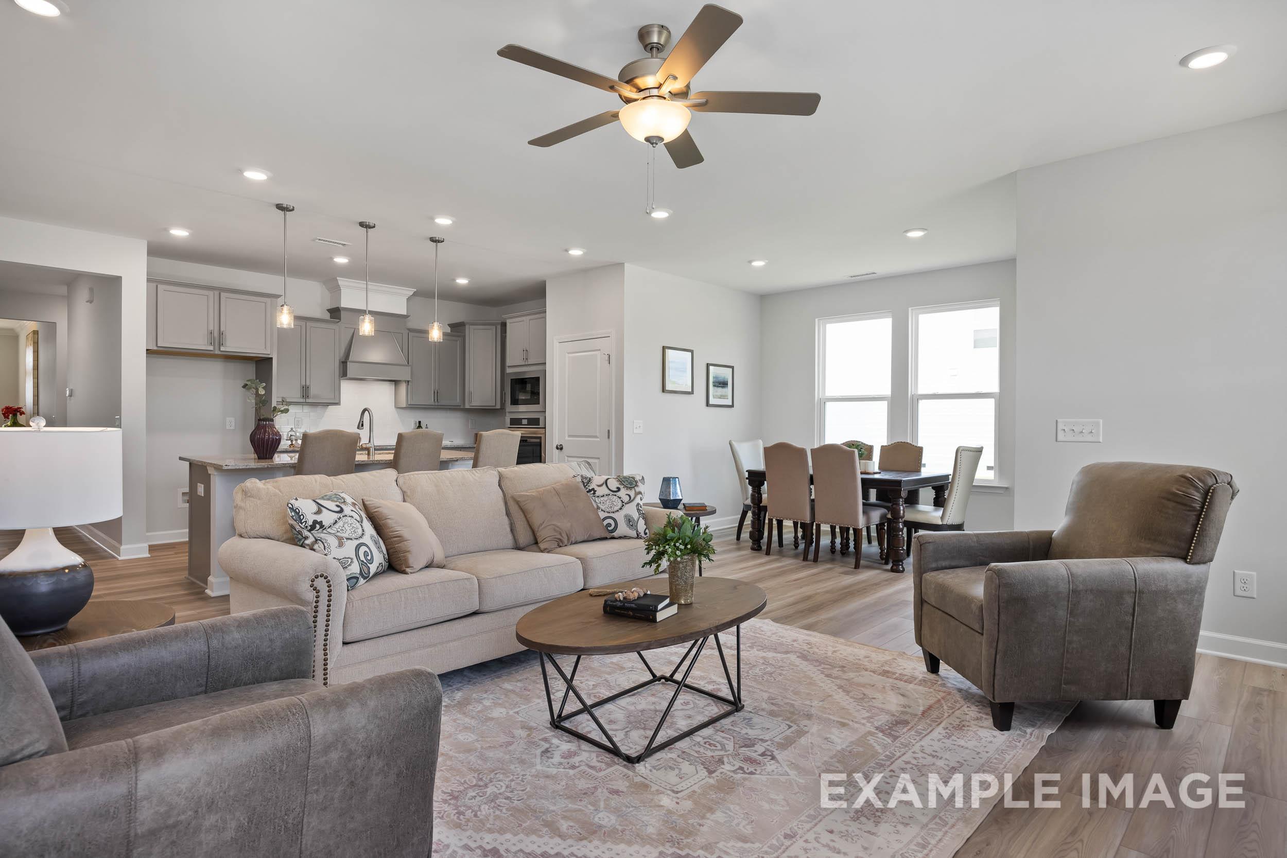 Spacious open-concept living and dining area in The Daphne C with gray sofa, wooden table, kitchen island, and ceiling fan