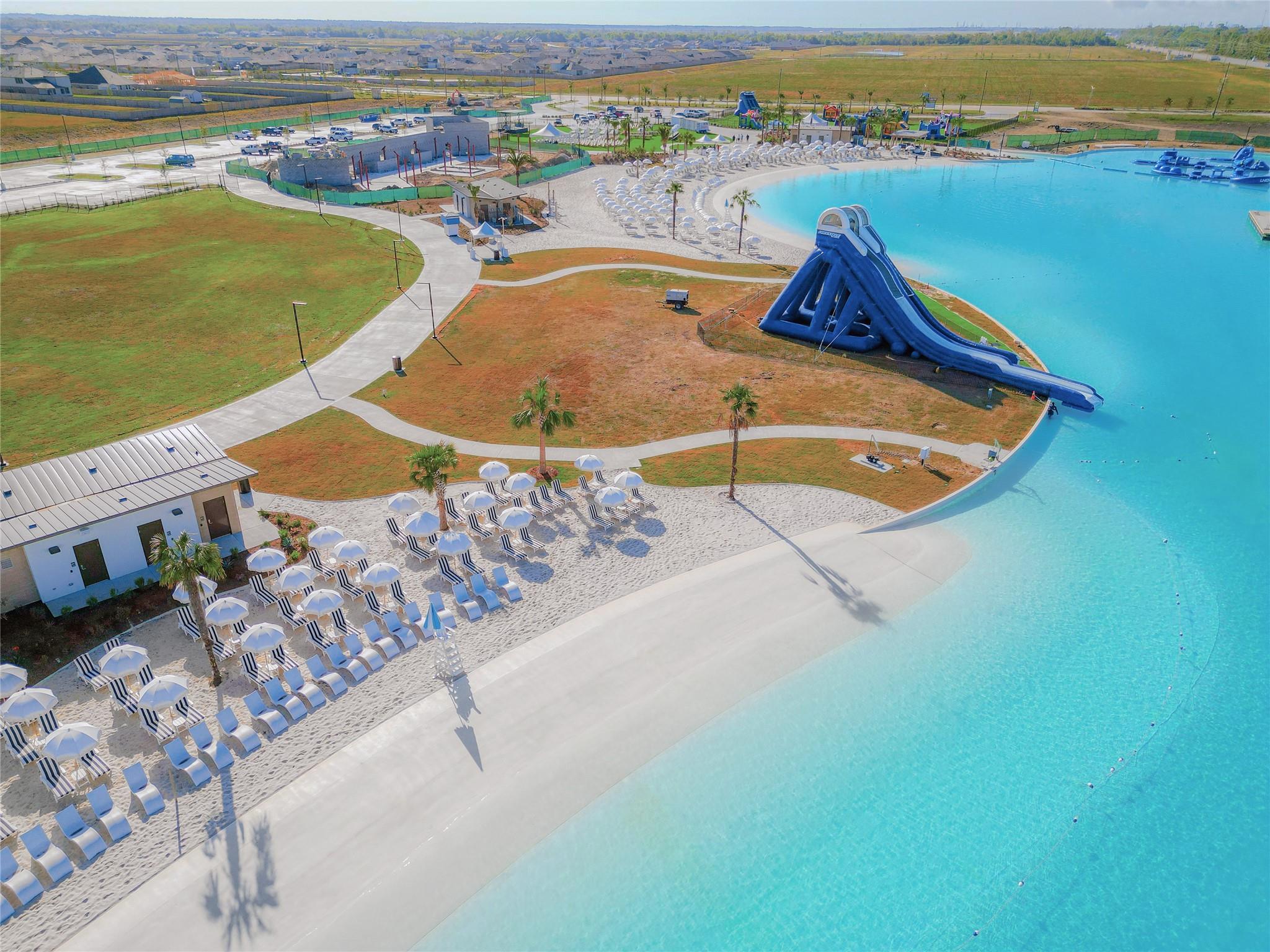 Crystal blue lagoon with waterslide and beach seating at River Ranch Meadows community near Dayton, Texas homes.
