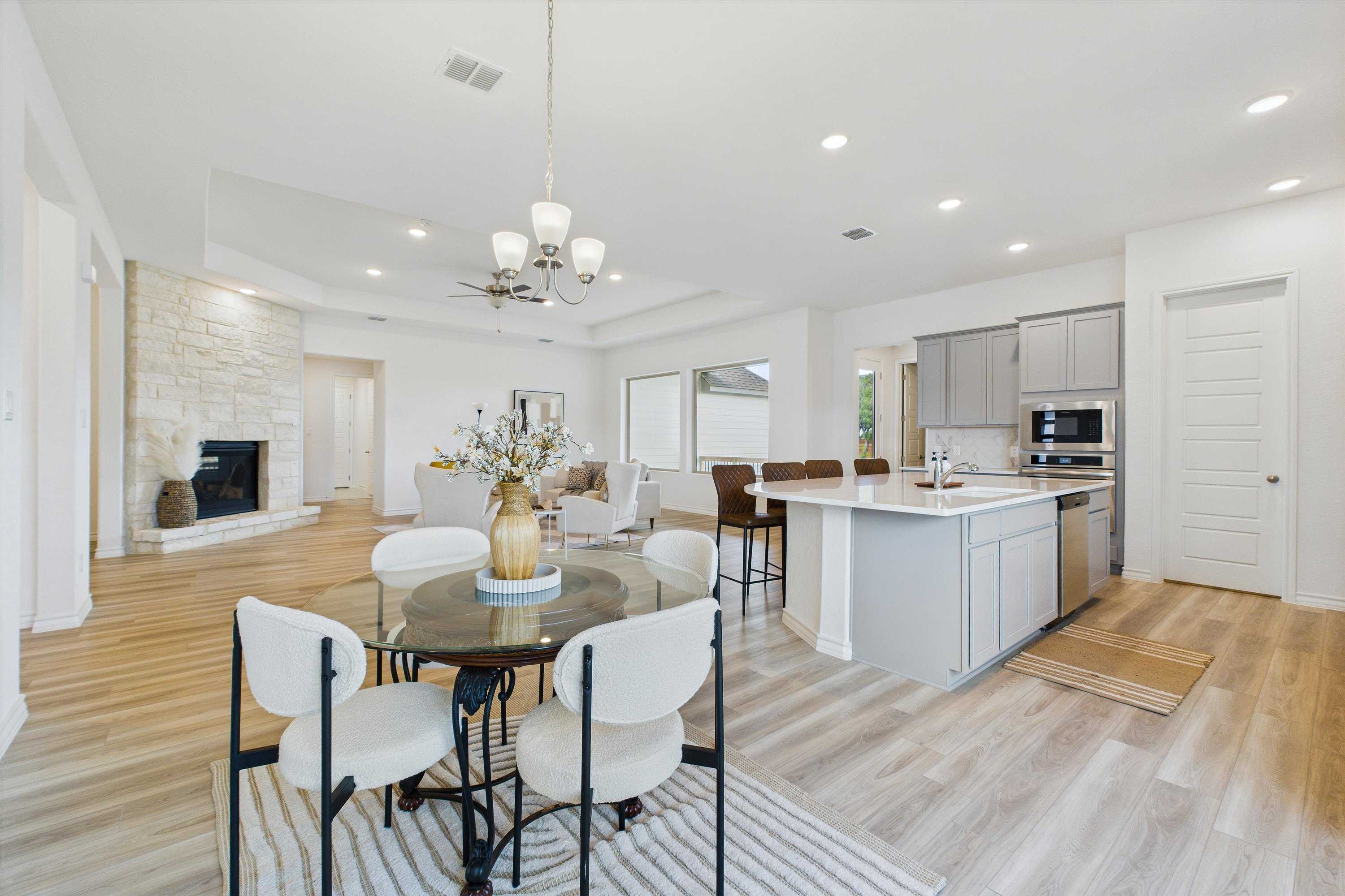 Open-concept living and kitchen with stone fireplace, white shaker cabinets, stainless appliances, and hardwood floors in The Summerlin C, Castroville, TX