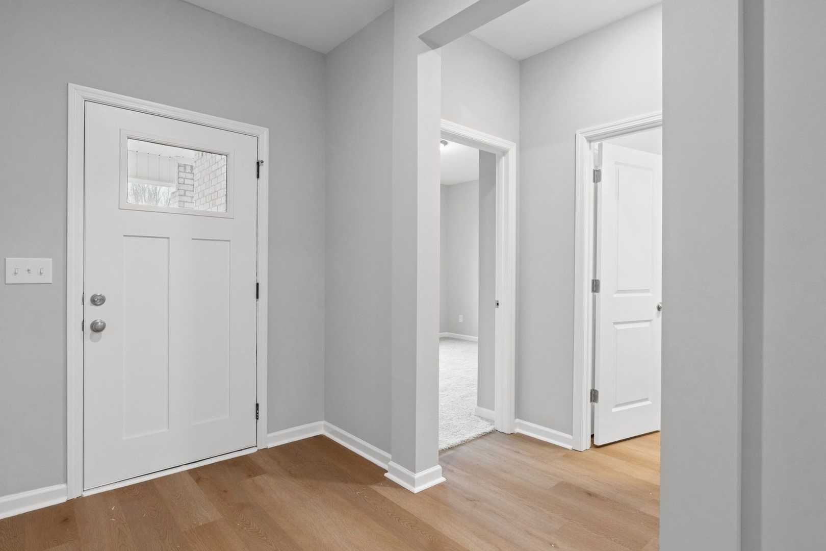 Spacious entryway in The Luna home with gray walls, white paneled doors, open archway, and hardwood floors