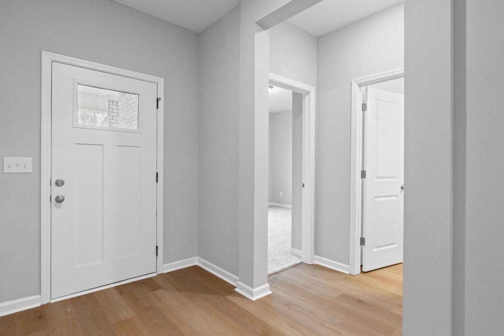 Spacious entryway in The Luna home with gray walls, white paneled doors, open archway, and hardwood floors