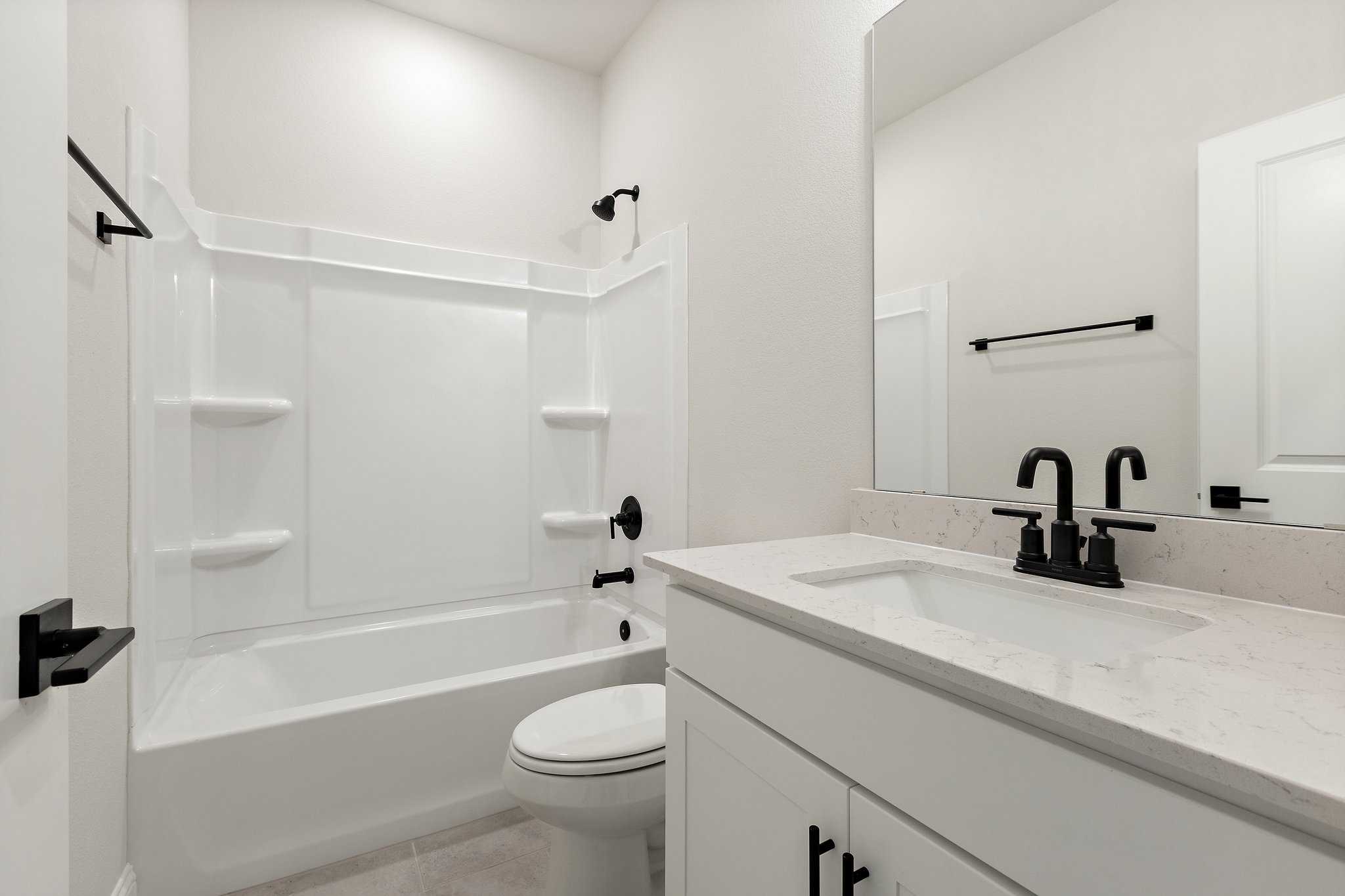 Spacious master bathroom in The Harrison C by Davidson Homes featuring white tub-shower combo, quartz vanity, and black fixtures