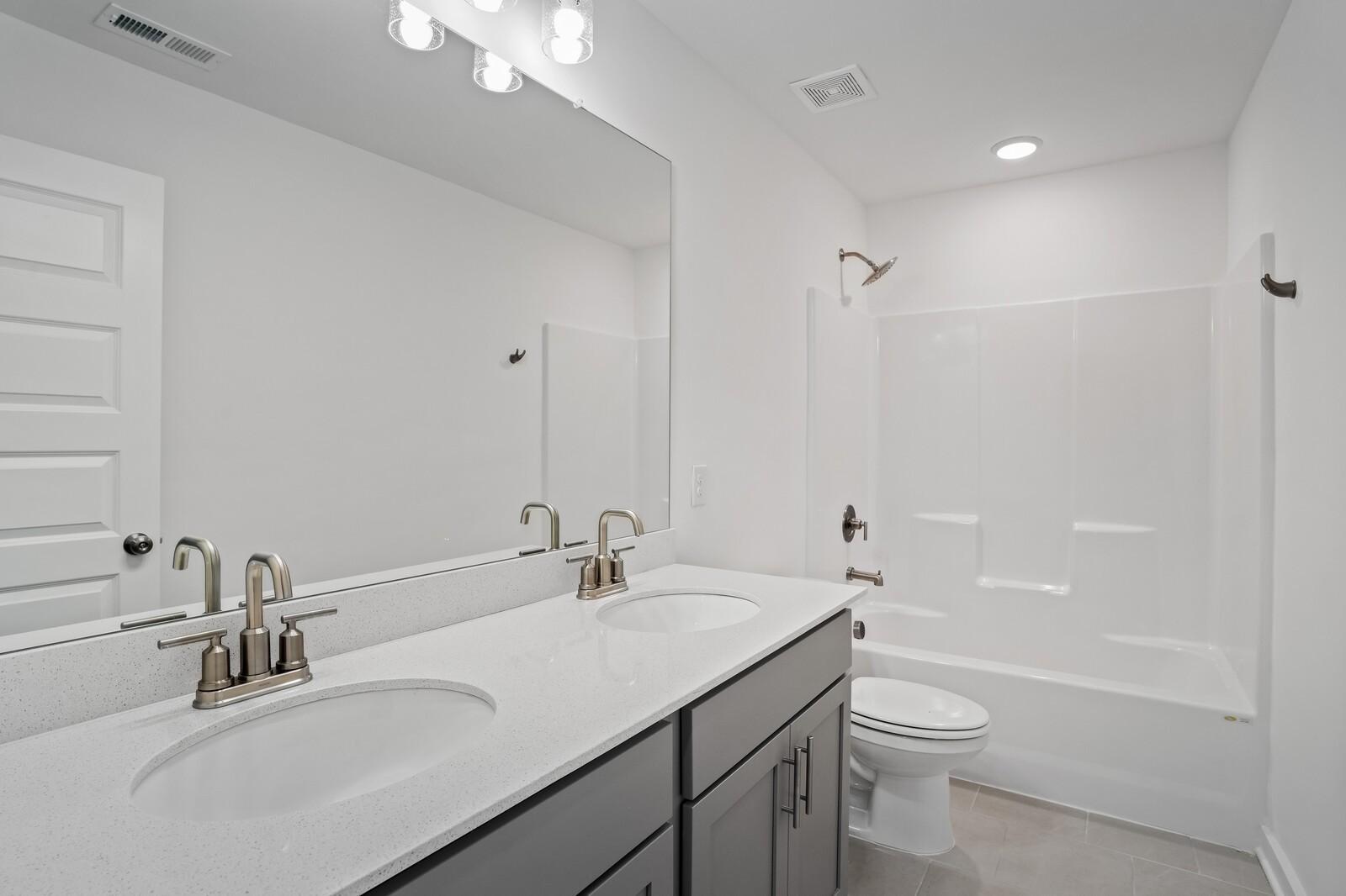 Modern bathroom with dual vanity, quartz countertops, and tub-shower combo in The Logan C home at Calista Farms, Tennessee.