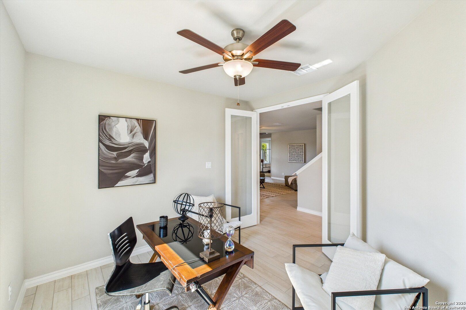 Modern home office with wooden desk, ceiling fan, French doors, and abstract art in Davidson Homes The Jennings H, Ladera, Texas