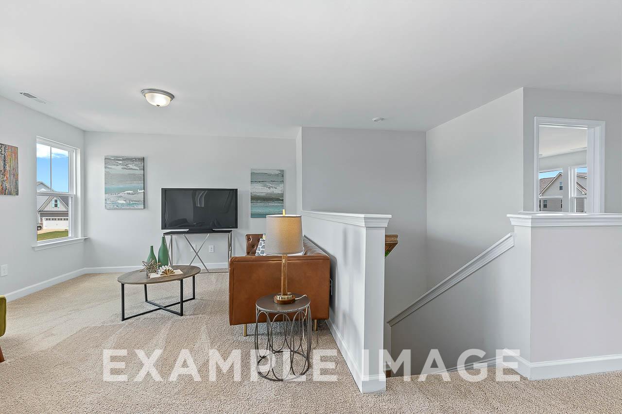 Spacious family room in The Willow C with leather sofa, TV console, open staircase, and large windows in Davidson Homes design