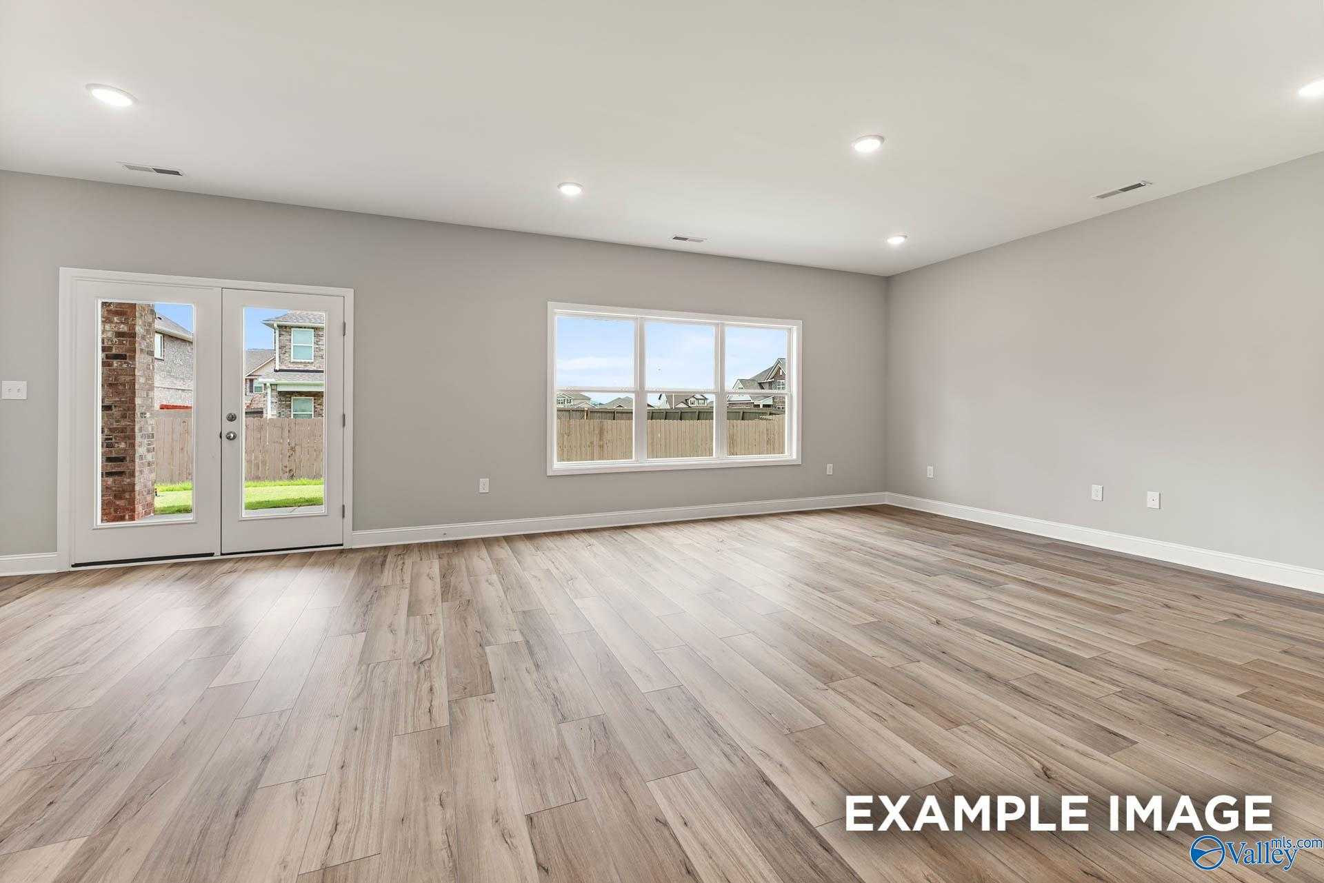 Bright living room with hardwood floors, large windows, and French doors to fenced backyard in The Chelsea A, Athens, Alabama