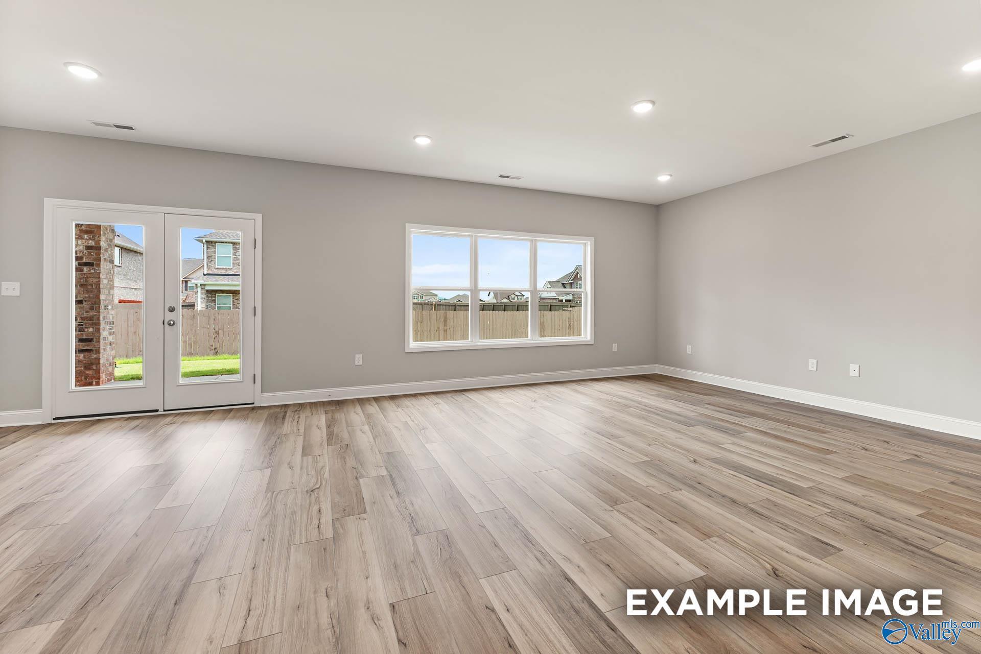 Spacious empty living room with light gray walls, hardwood floors, French doors to fenced backyard in Davidson Homes Chelsea B, Toney, AL