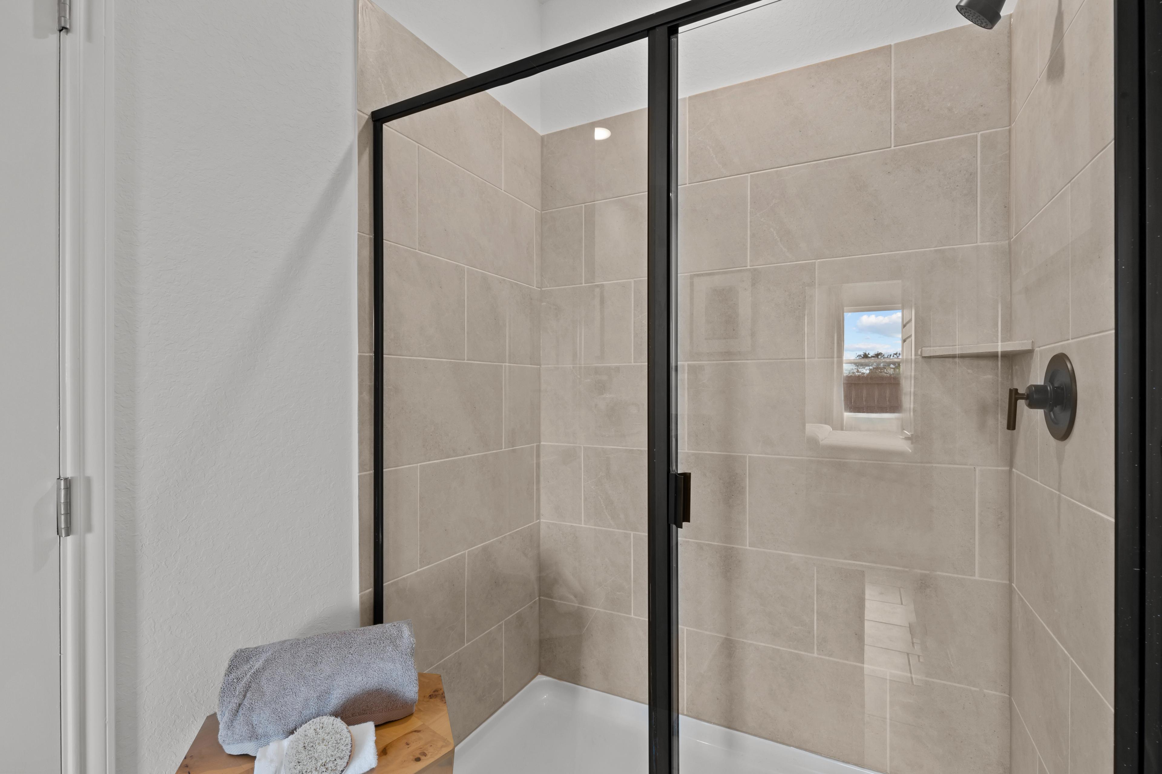 Frameless glass shower in The Douglas F master bath with beige subway tiles, rainfall showerhead, and window for natural light
