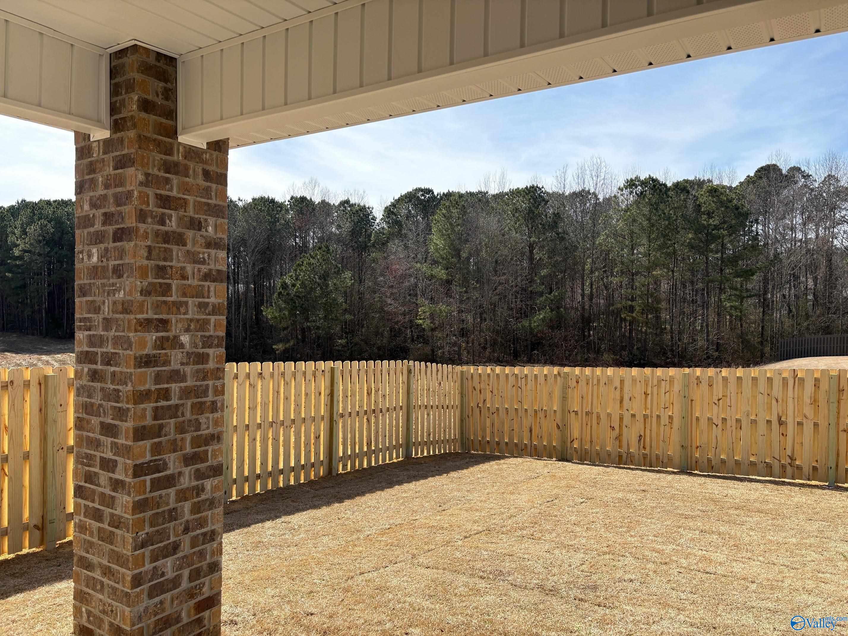 Covered back patio with brick pillar and wooden fence overlooking wooded yard in The Daphne C, The Highlands, Arab, Alabama