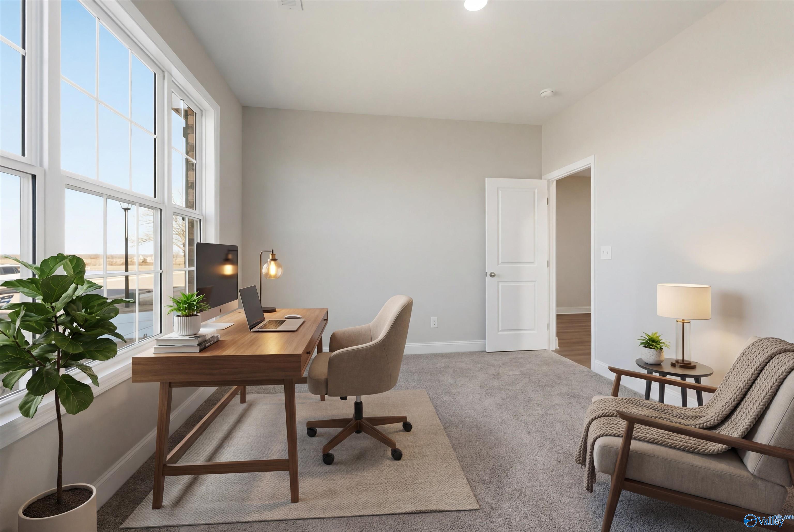 Modern home office with wooden desk, laptop, potted plant, and large windows in Davidson Homes The Montgomery B, Toney, Alabama