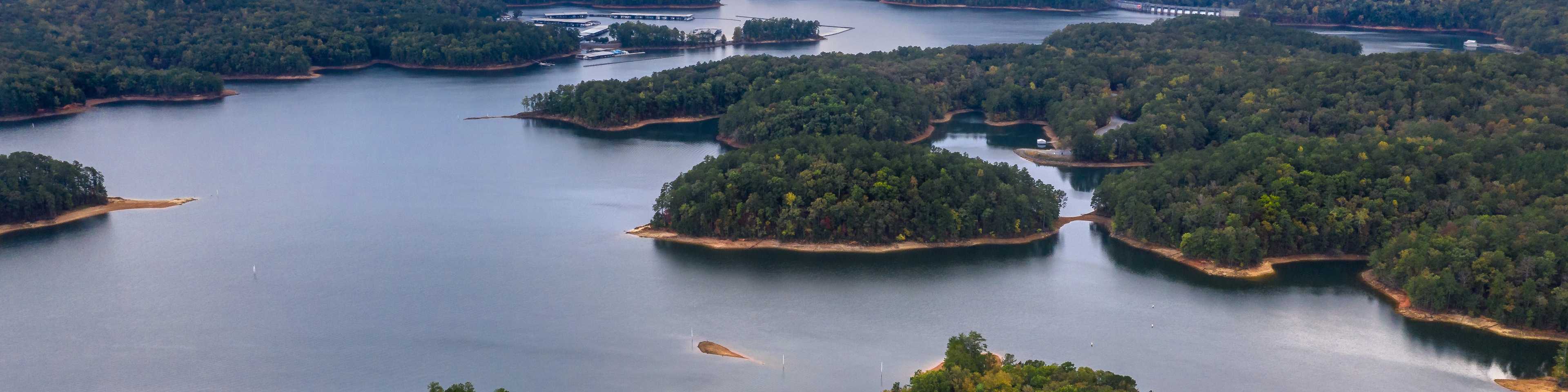 Aerial view of serene lake with forested islands, docks, and waterfront homes in Grafton Trace, Woodstock, Georgia