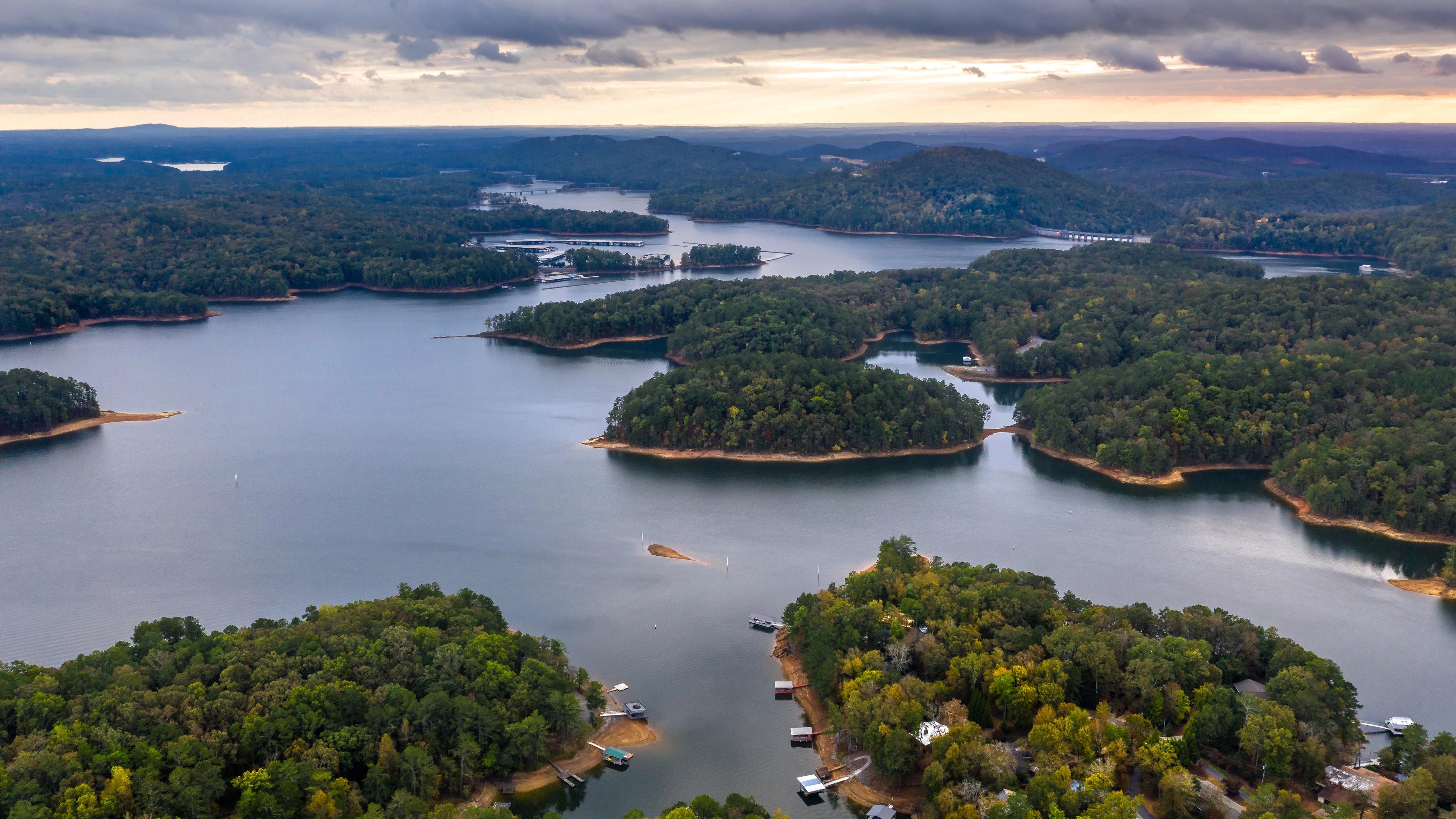 Aerial view of serene lake with forested islands, docks, and waterfront homes in Grafton Trace, Woodstock, Georgia