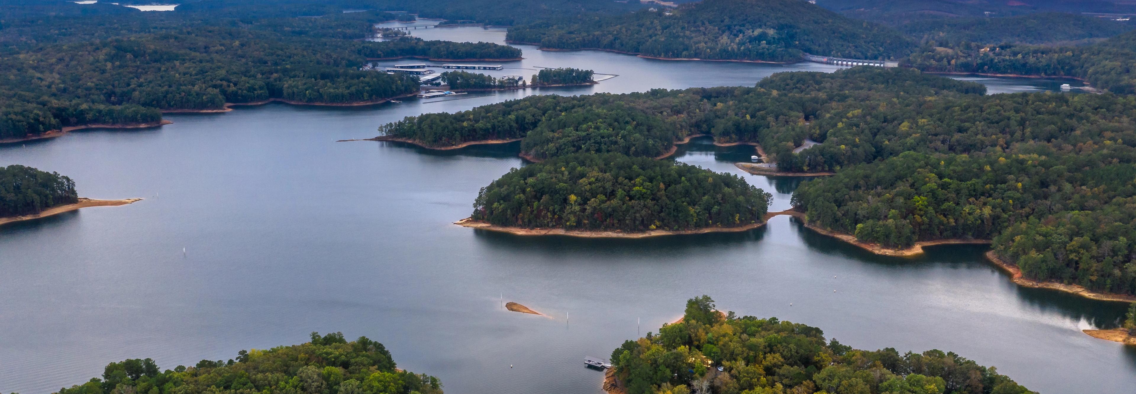 Aerial view of serene lake with forested islands, docks, and waterfront homes in Grafton Trace, Woodstock, Georgia
