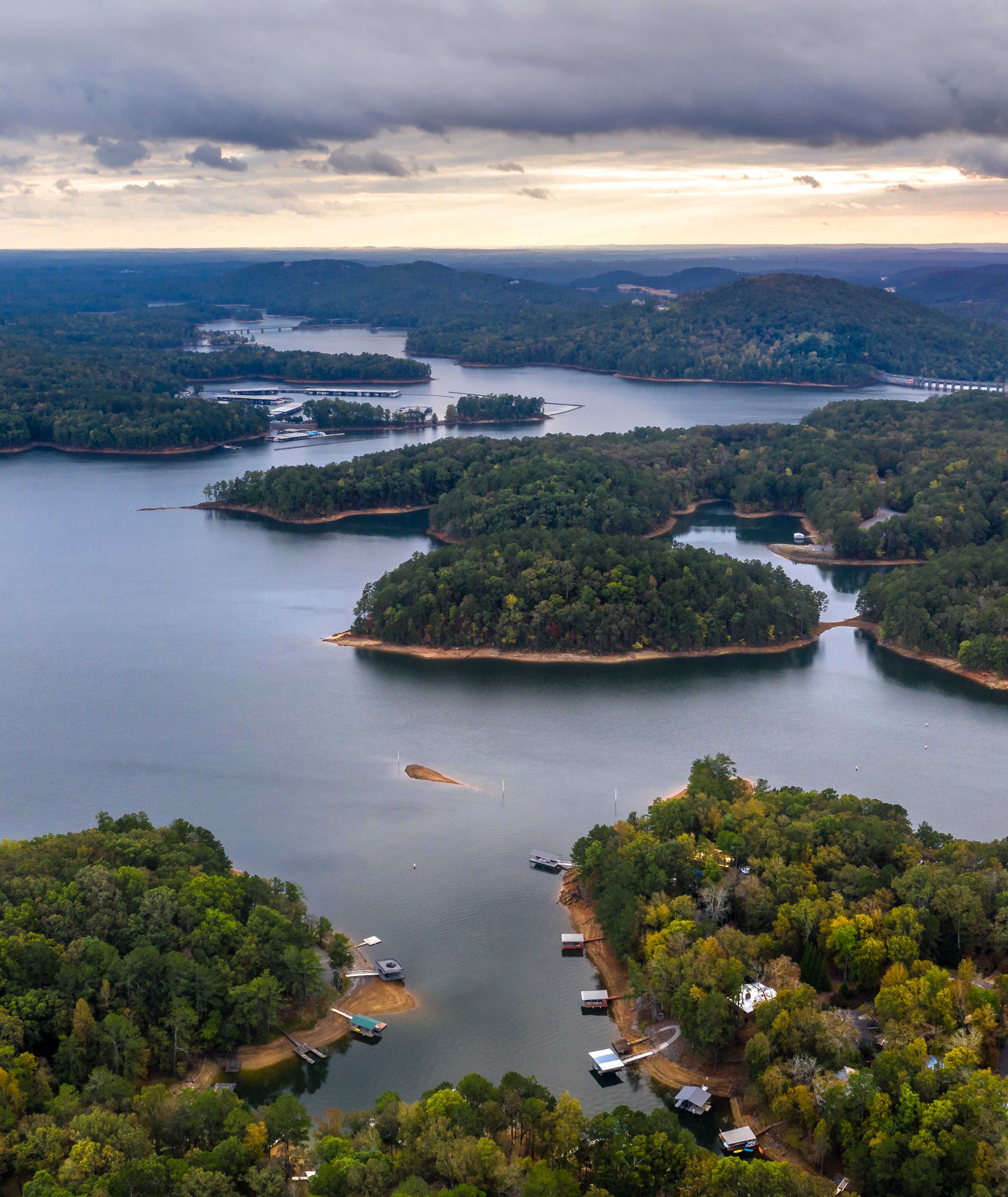 Aerial view of serene lake with forested islands, docks, and waterfront homes in Grafton Trace, Woodstock, Georgia