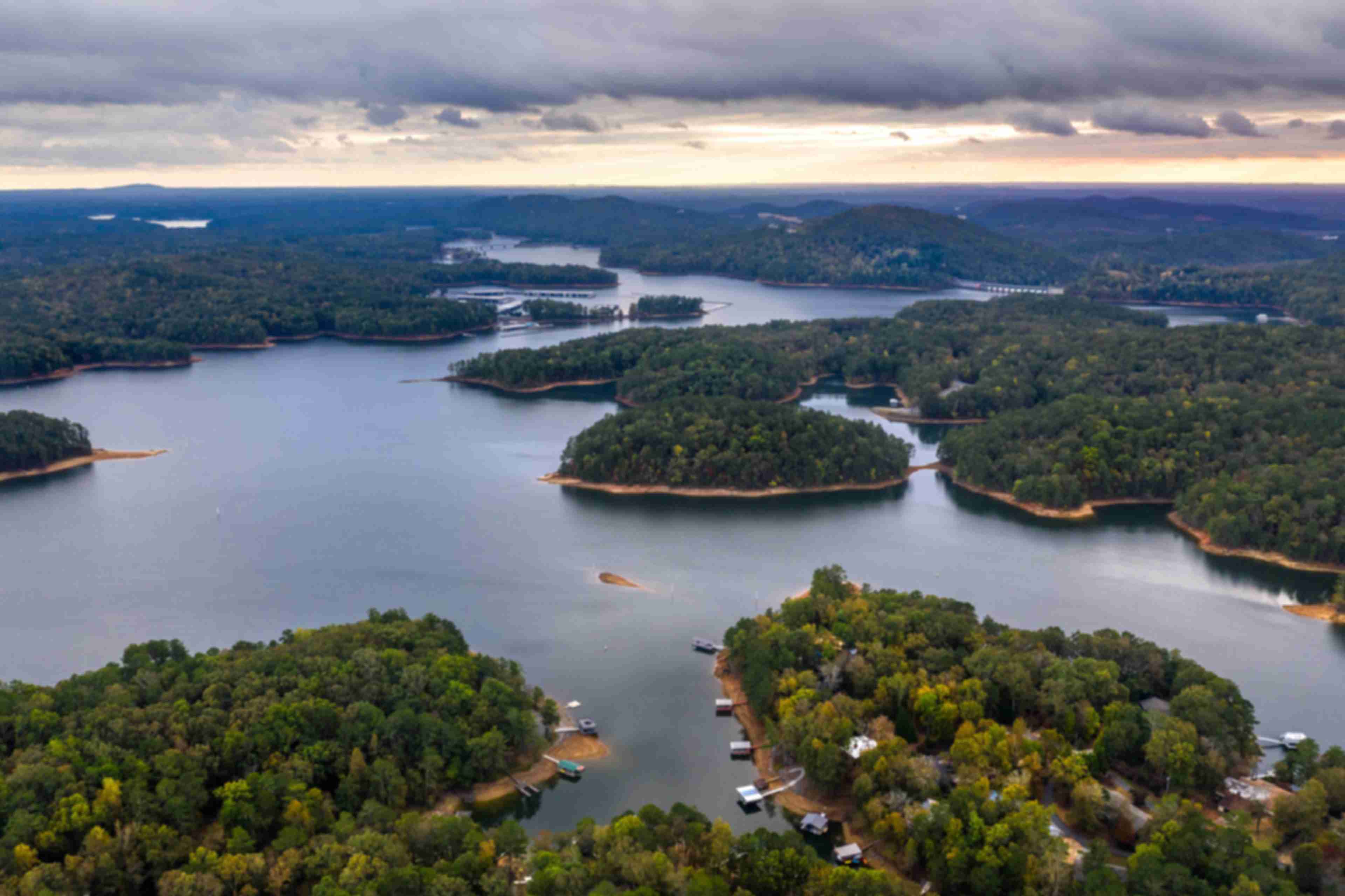 Aerial view of serene lake with forested islands, docks, and waterfront homes in Grafton Trace, Woodstock, Georgia