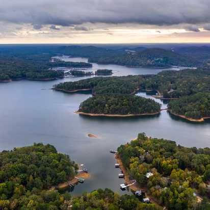 Aerial view of serene lake with forested islands, docks, and waterfront homes in Grafton Trace, Woodstock, Georgia
