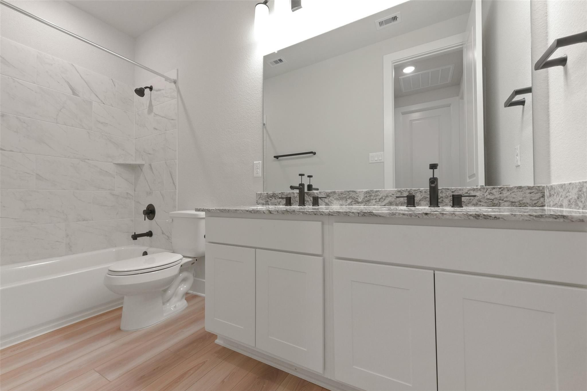 Modern master bathroom with double quartz vanity, marble shower, tub, and black fixtures in Davidson Homes The Edward C, Lago Mar, Texas