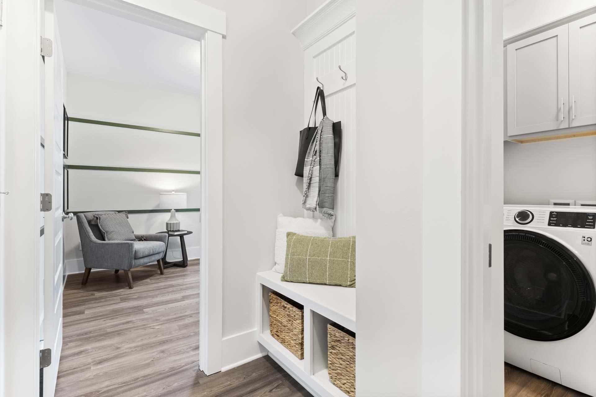 Spacious mudroom laundry in The Meadows Athens AL home with white cabinetry built-in bench wicker baskets washer dryer