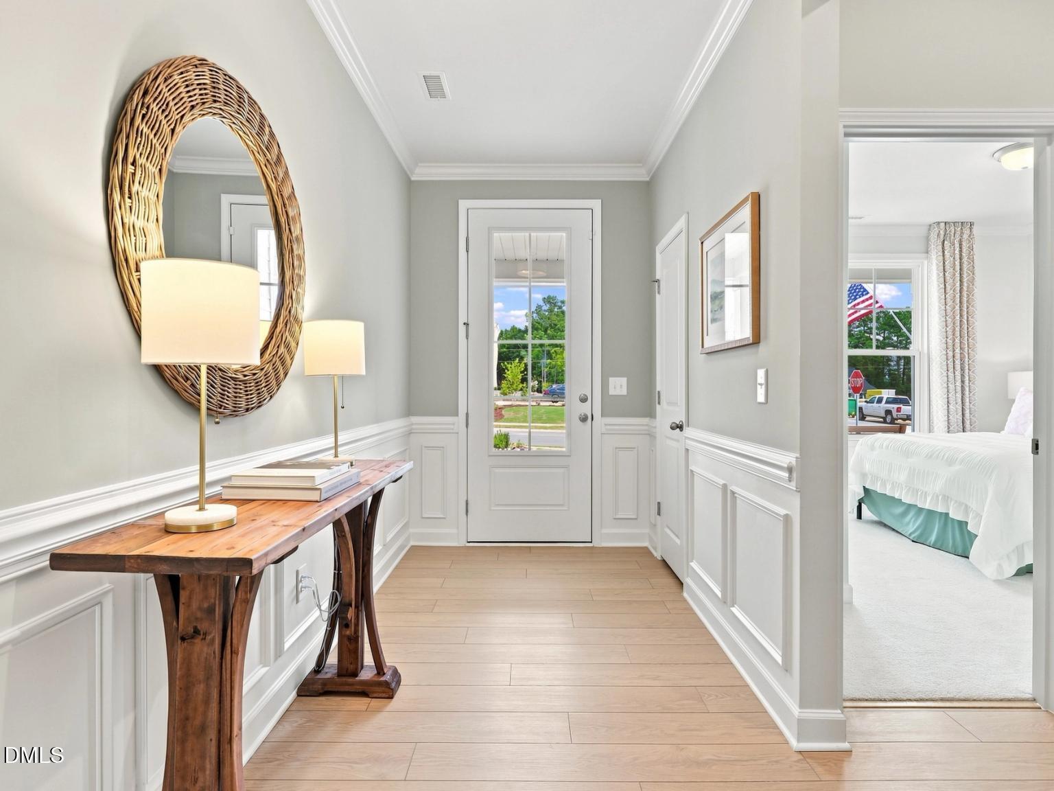 Bright foyer with wainscoting, wood console table, and round mirror in The Daphne C floor plan by Davidson Homes in Zebulon.