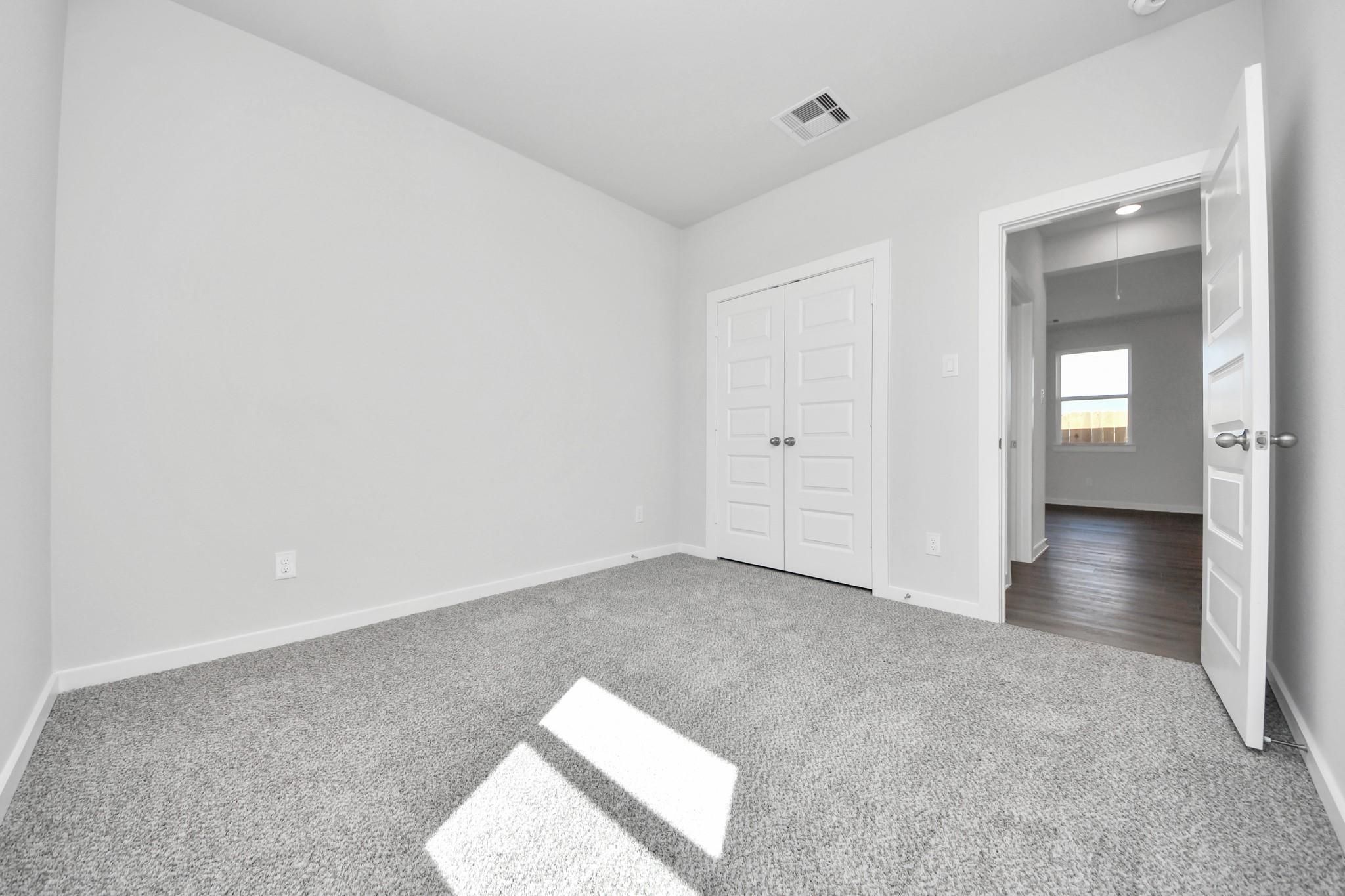 Bright secondary bedroom with carpet and double-door closet in The Riviera A floor plan at Emberly, Beasley, Texas.
