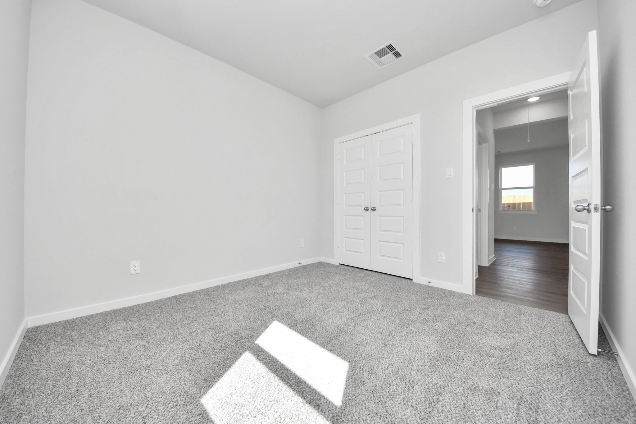 Bright secondary bedroom with carpet and double-door closet in The Riviera A floor plan at Emberly, Beasley, Texas.