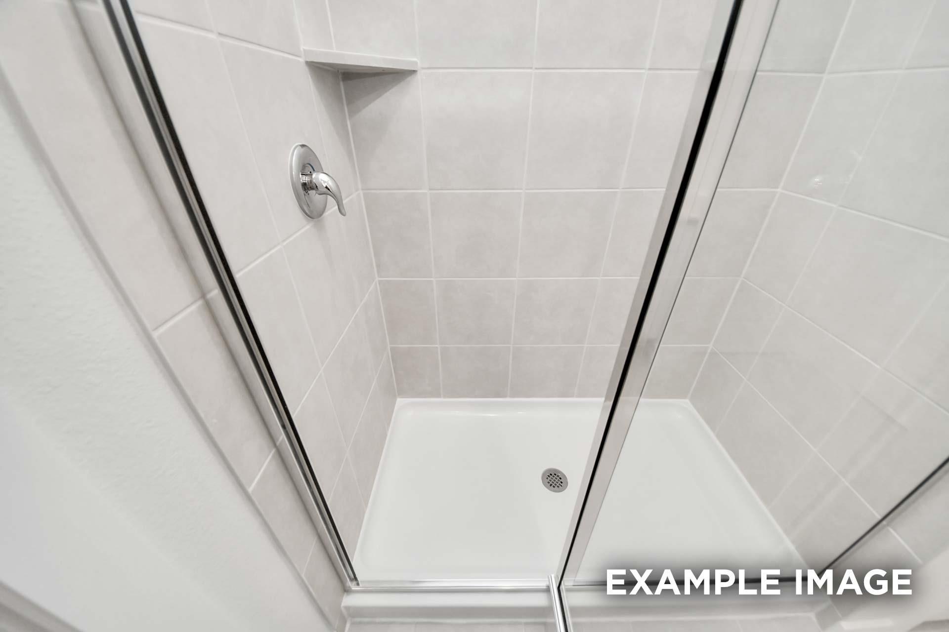 White tiled walk-in shower with sliding glass doors and built-in shelf in The Blanco E at Windmill Estates, Magnolia, Texas