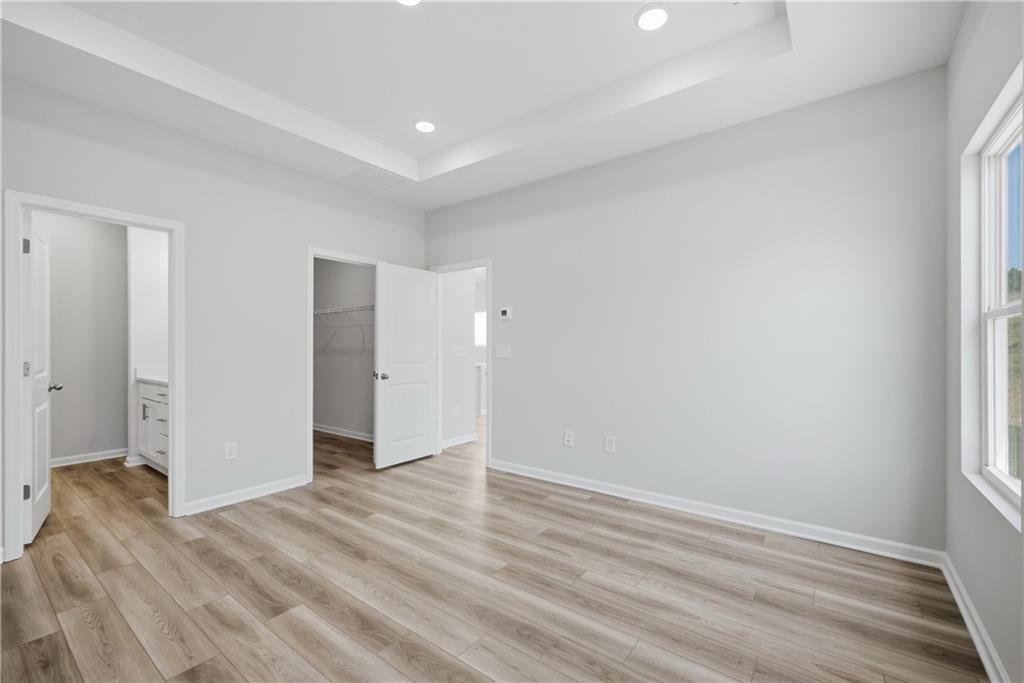 Bright primary bedroom with tray ceiling, LVP flooring, and walk-in closet in The Oconee B by Davidson Homes, Canton, GA