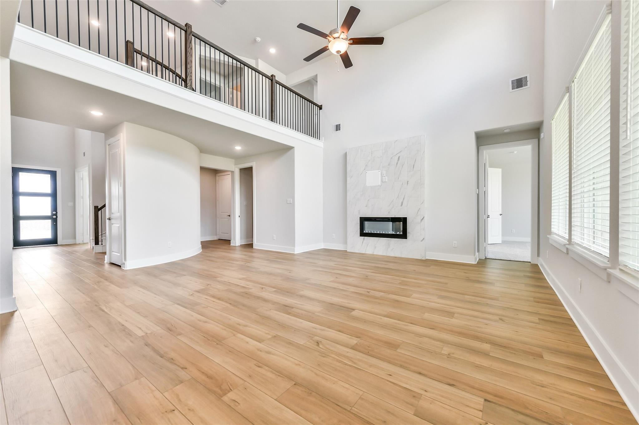 Grand two-story living room with wrought-iron balcony, linear marble fireplace, ceiling fans, and oak hardwood floors in Davidson Homes The Victoria A