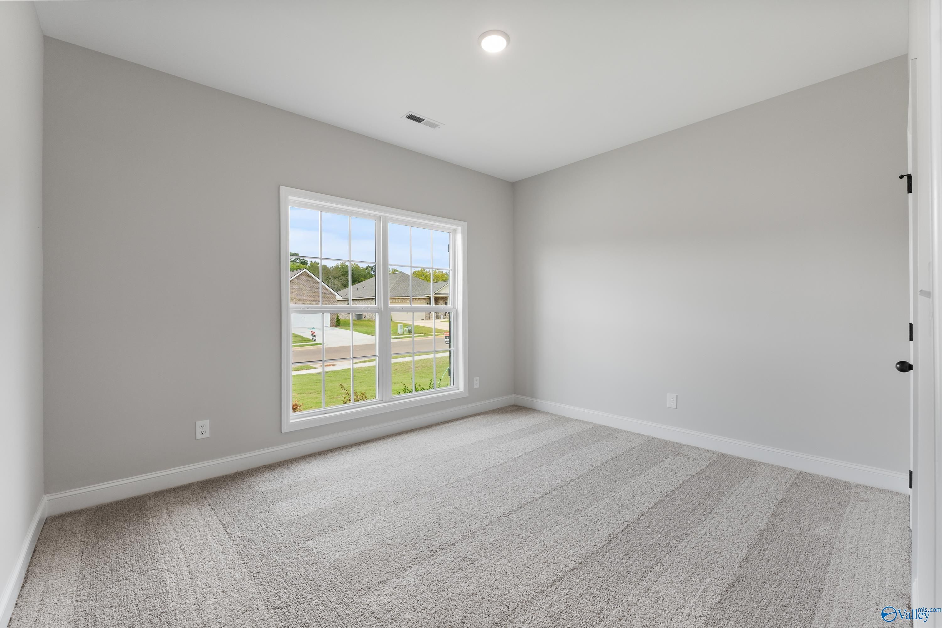 Bright empty bedroom with gray walls, beige carpet, and large window view of neighborhood in Davidson Homes The Daphne, Huntsville AL