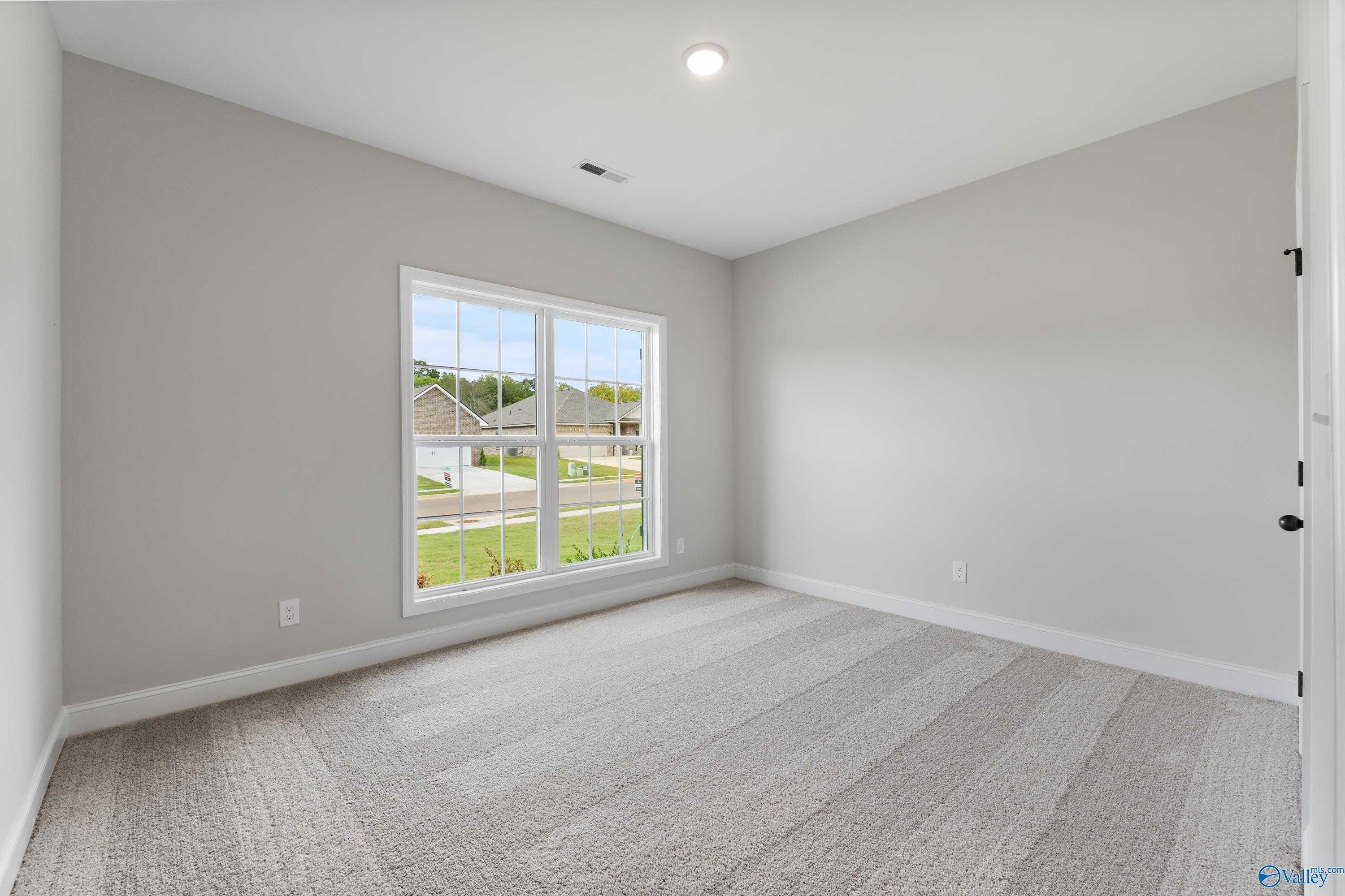 Bright empty bedroom with gray walls, beige carpet, and large window view of neighborhood in Davidson Homes The Daphne, Huntsville AL