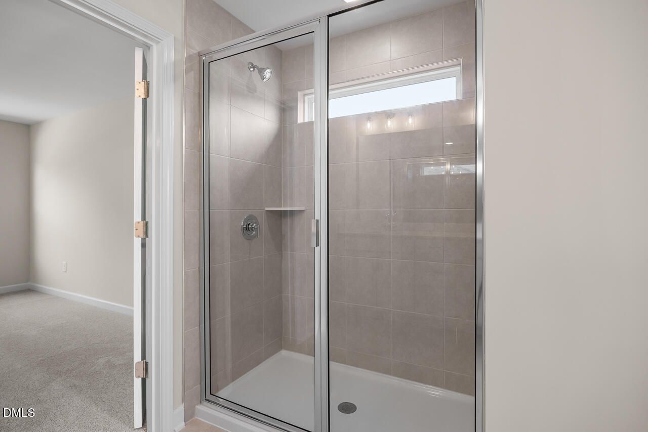 Frameless glass tile shower with transom window in bathroom of Davidson Homes The Willow C, Zebulon, North Carolina