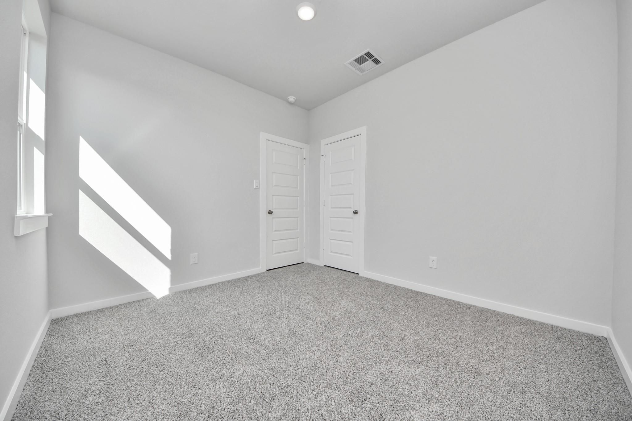 Bright, carpeted bedroom with white walls and two closet doors in The Colorado G floor plan at Emberly in Beasley, Texas.