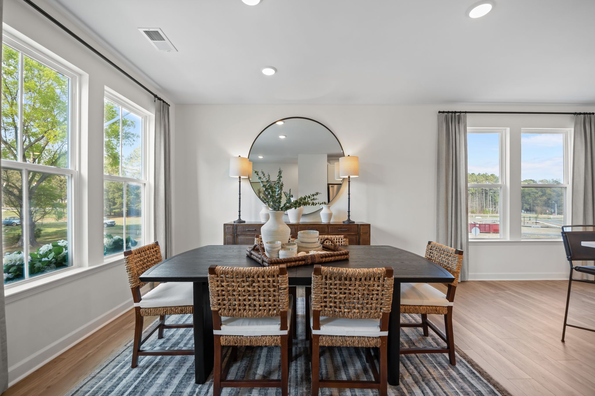 Bright dining room in The Mitchell interior design featuring a dark wood table, woven chairs, and large windows.