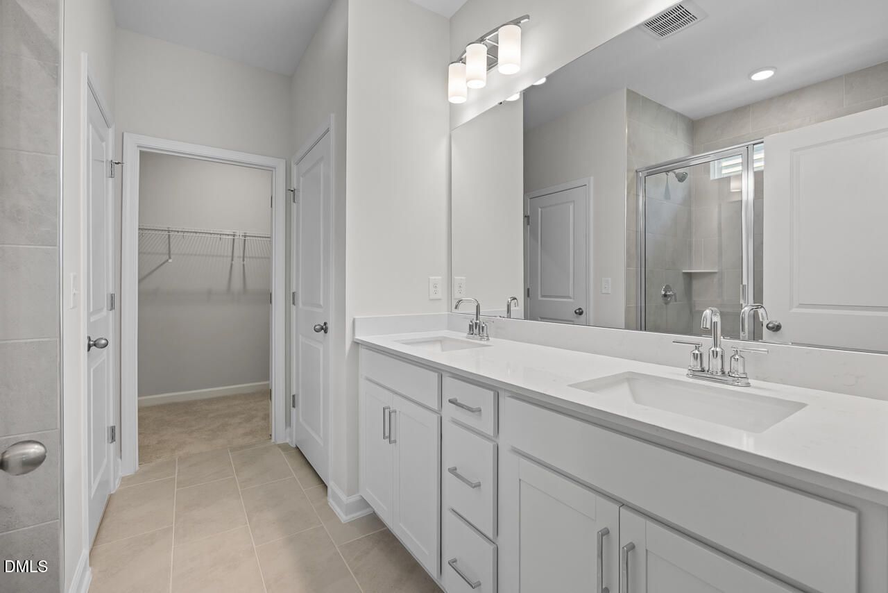 Double vanity bathroom with white cabinetry, walk-in closet, and tile shower in Davidson Homes The Daphne D, Zebulon NC