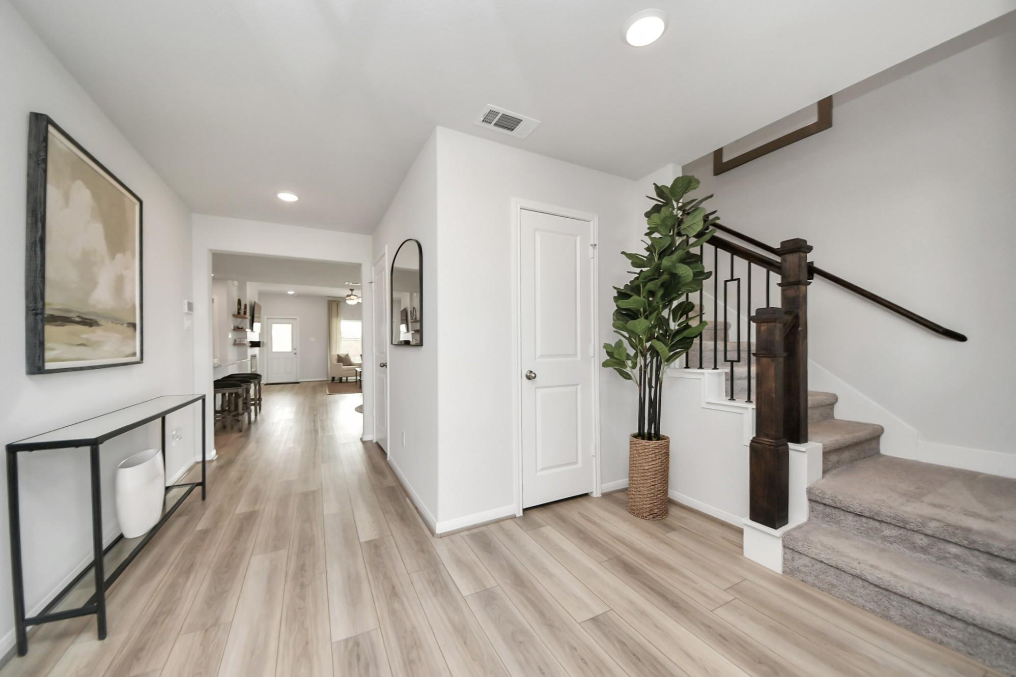 Bright entryway with modern staircase, wood-look flooring, and decor at Sunterra in Katy, TX by Davidson Homes.