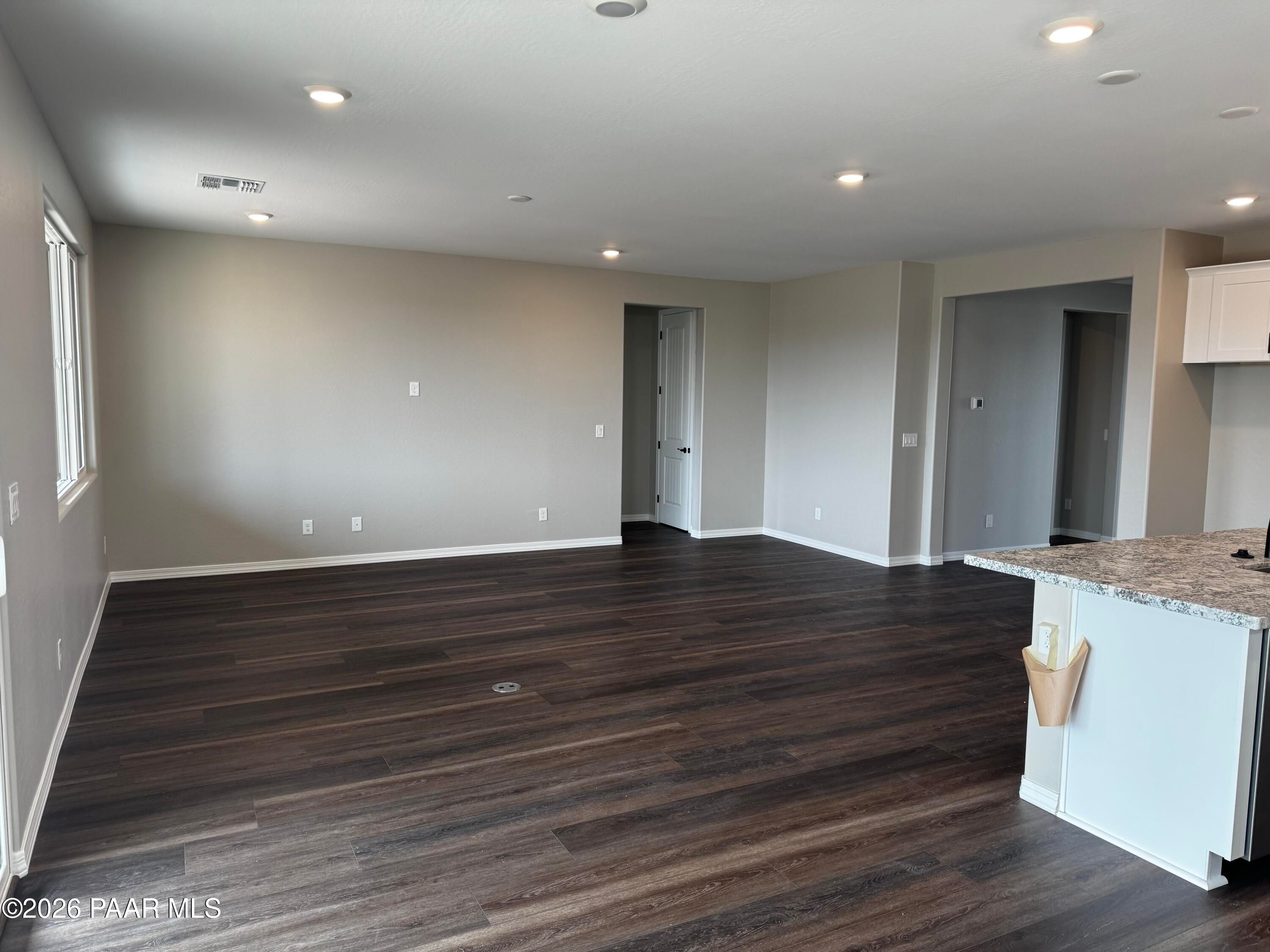 Open living room with hardwood floors, beige walls, recessed lights, and adjacent kitchen island in The Durango II B, Prescott, AZ