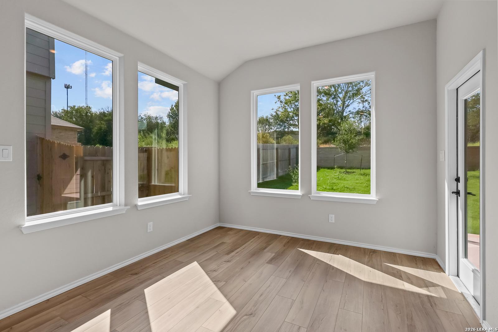 Bright sunlit room with wood-look flooring and large windows overlooking fenced backyard in Davidson Homes Sequoia C, San Antonio
