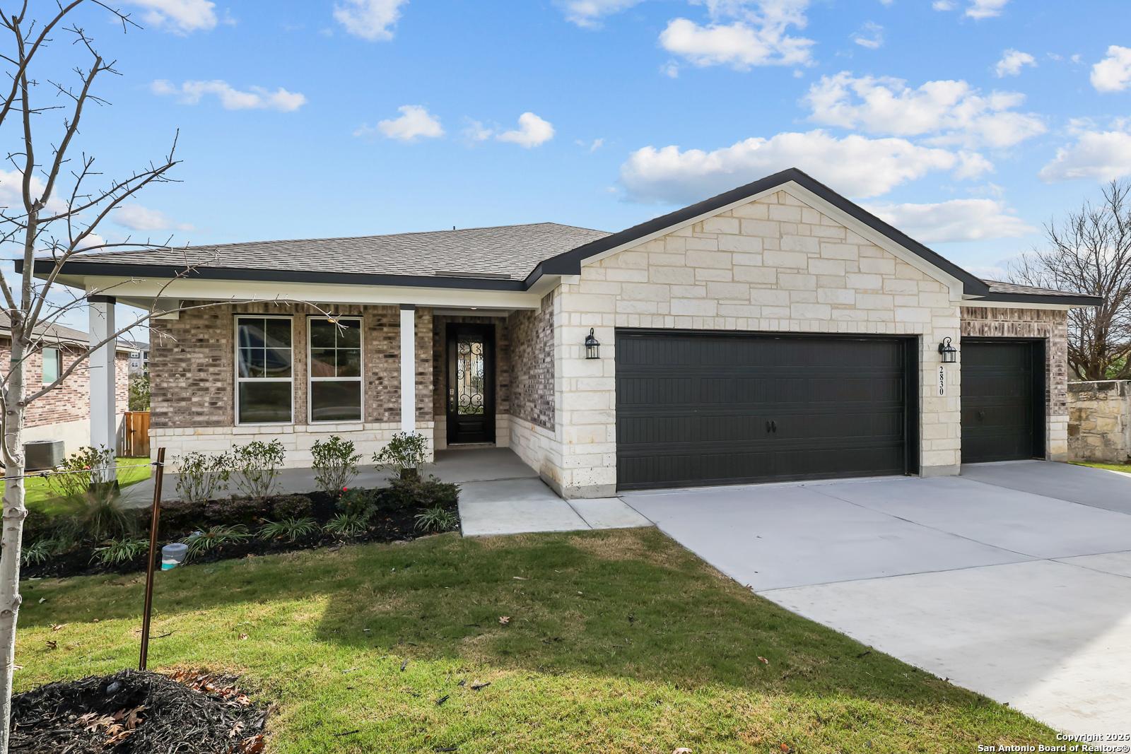 Modern single-story home with beige brick and stone facade, 3-car black garage, landscaped front yard in Ladera, San Antonio, Texas - Davidson Homes Lanier H