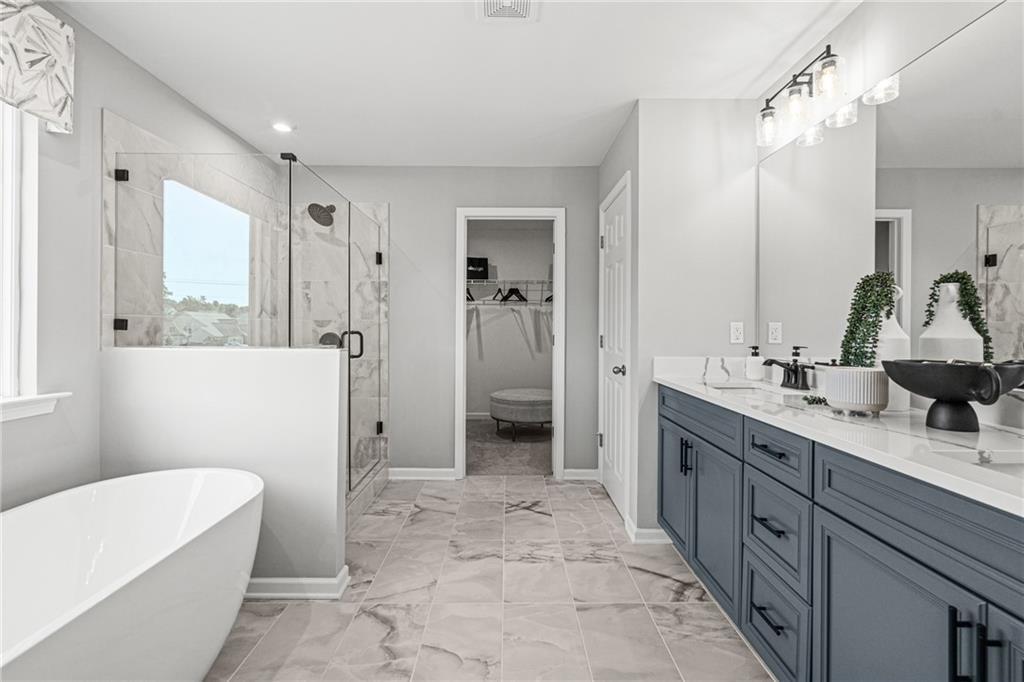 Modern primary bathroom with soaking tub, glass shower, and navy double vanity in The Hickory A at Wehunt Meadows, Hoschton.
